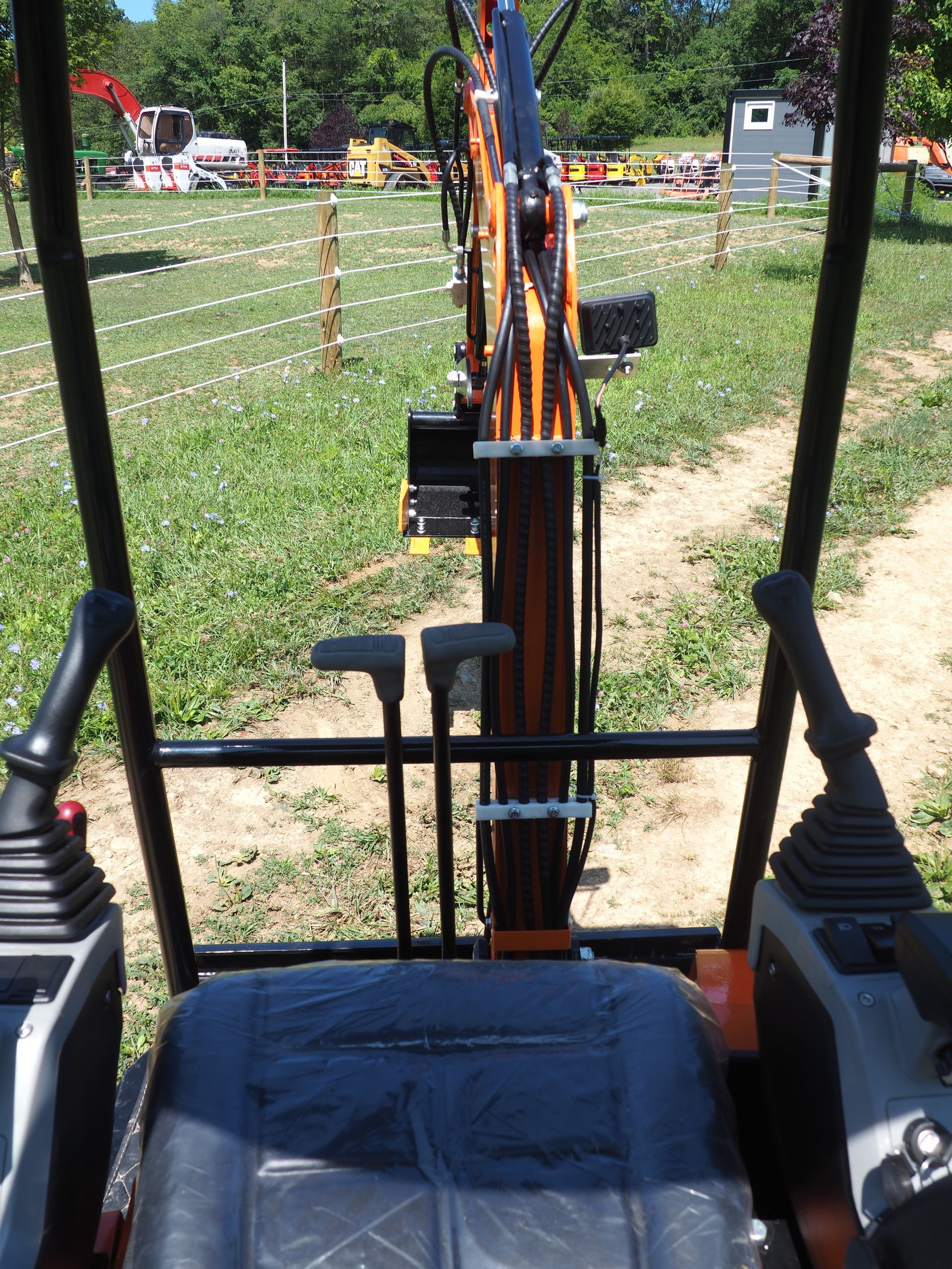 Interior view of excavator cab, showing controls, seat, and the boom extending into an outdoor construction site.