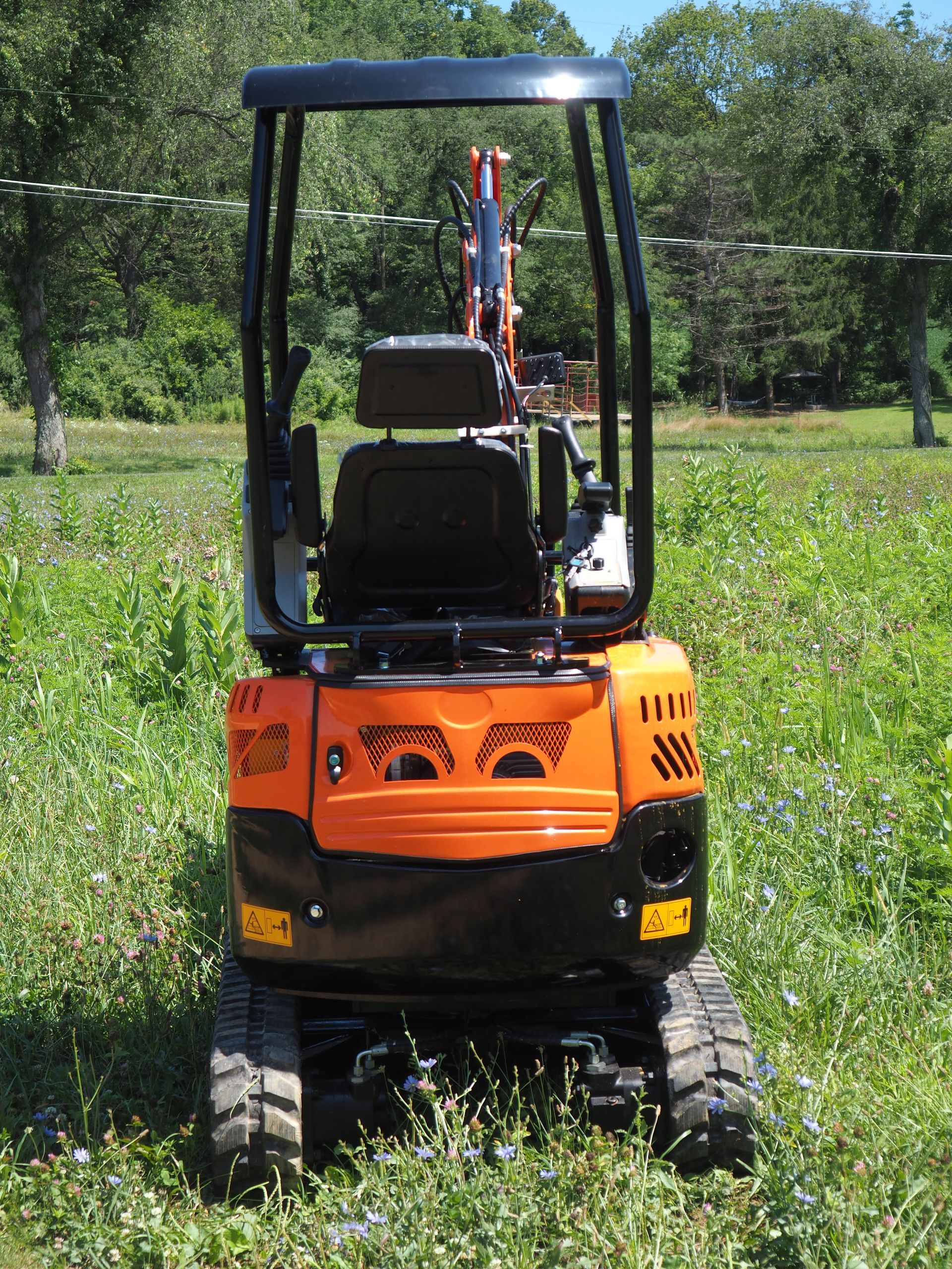 Orange and black mini-excavator on tracks in a grassy field, with a roll cage.