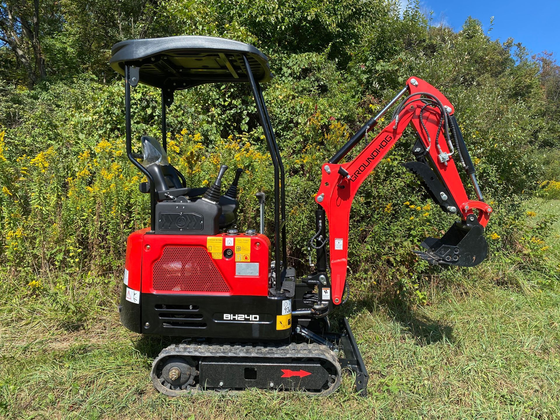 Red and black mini excavator on grass, with a black canopy.