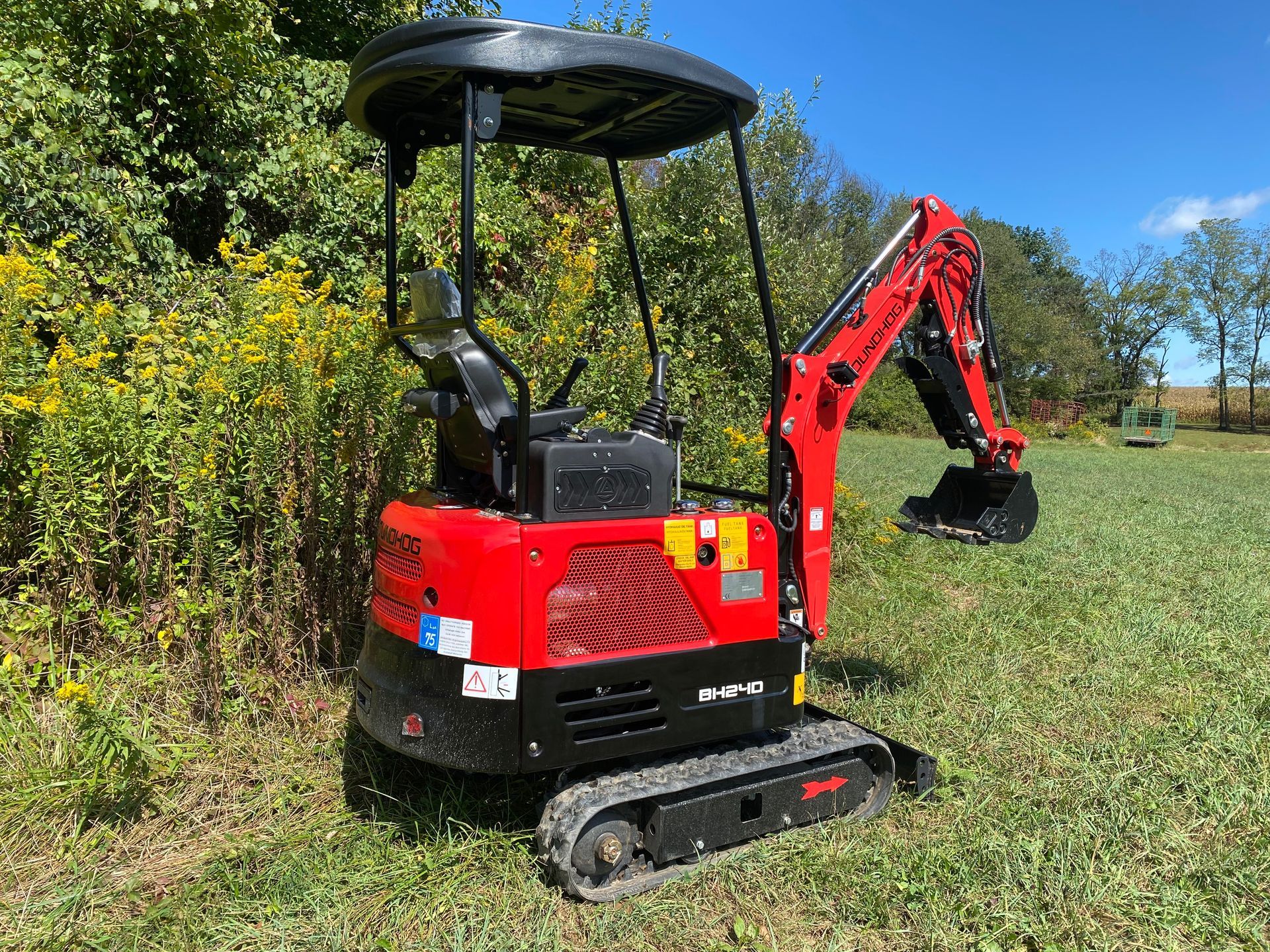 Red mini excavator on tracks in a grassy field.