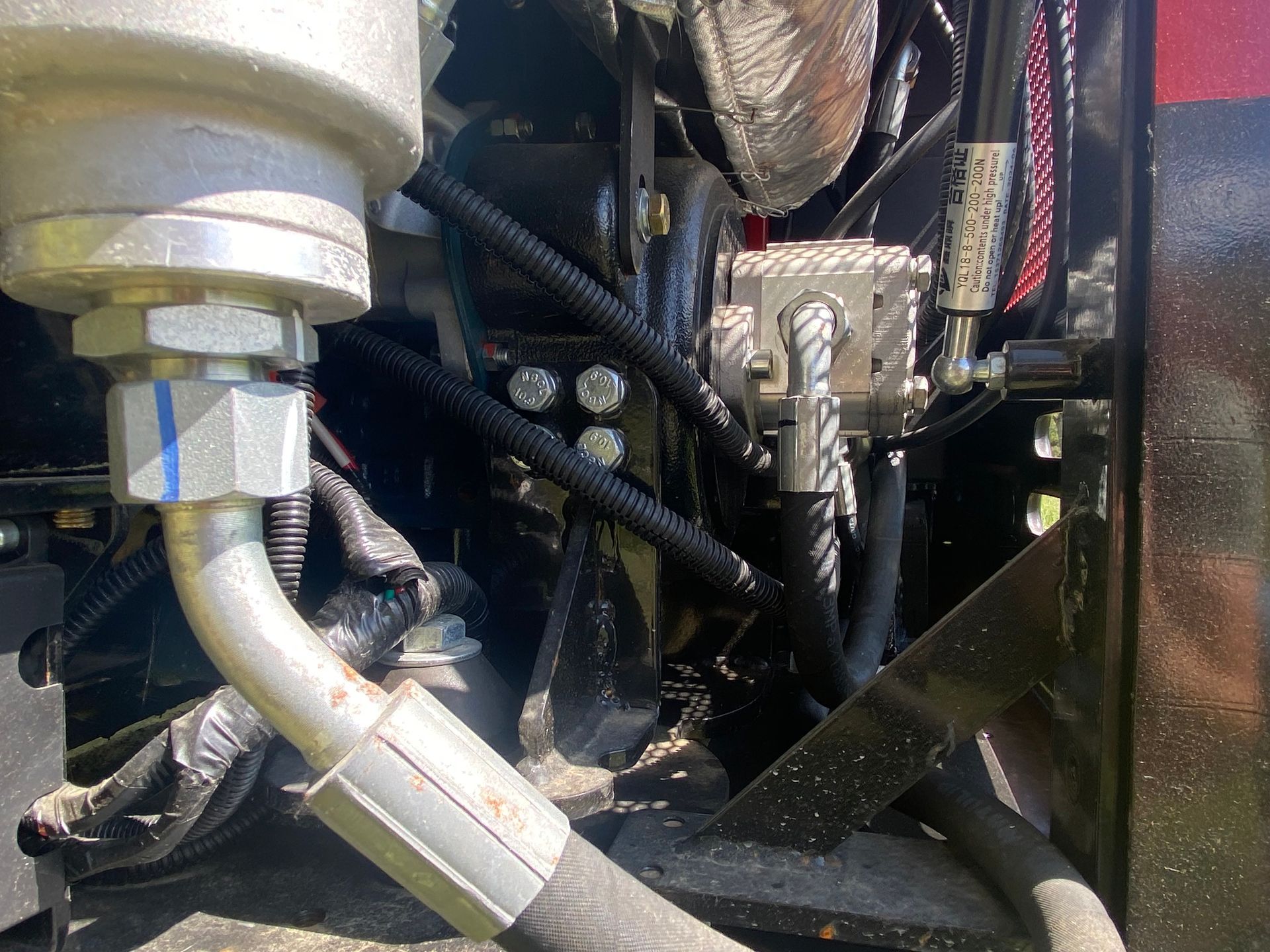 Close-up view of a tractor engine's hydraulic system with metal tubing, hoses, and black wiring.