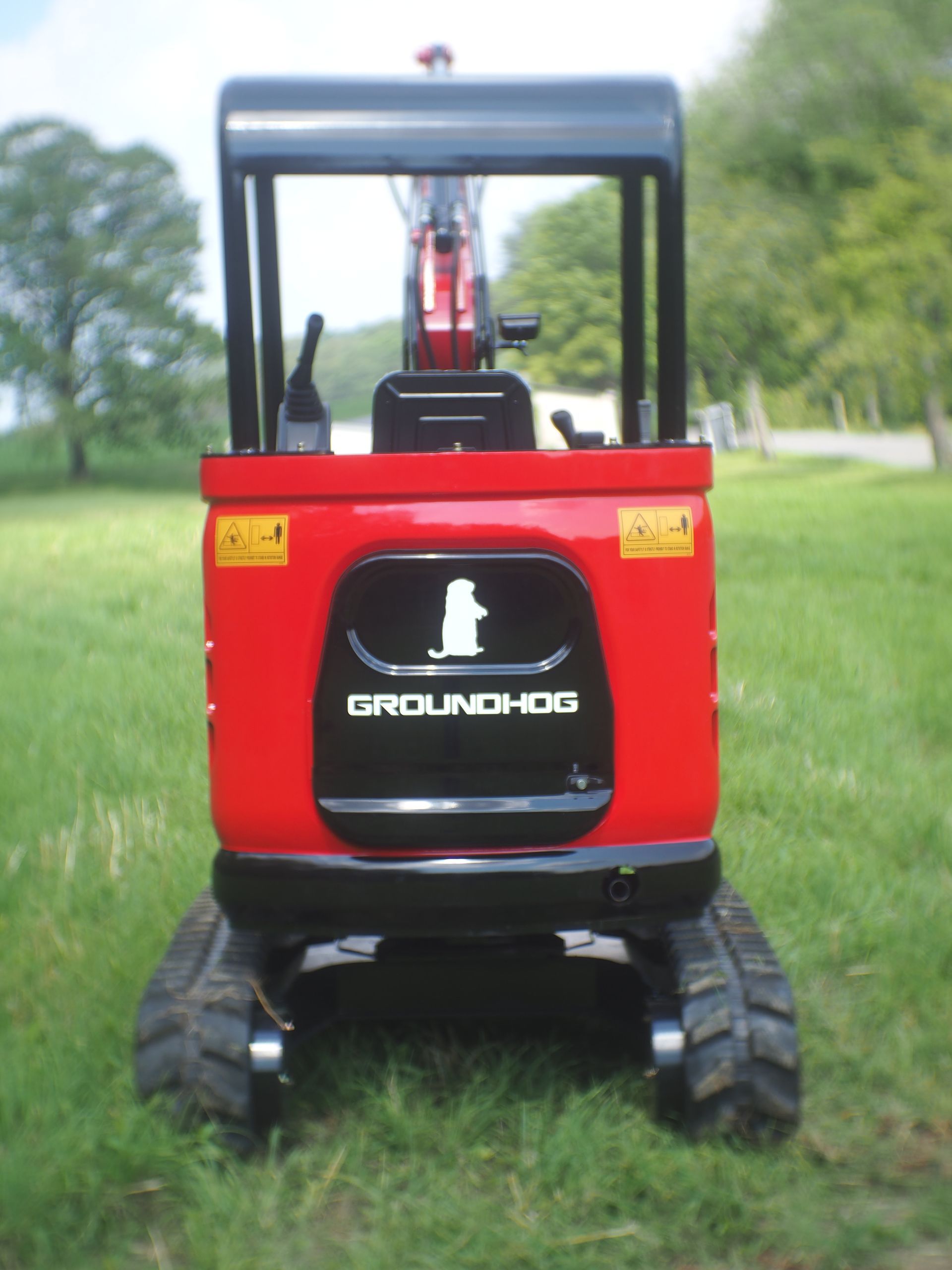 Red and black Groundhog mini excavator on grass.