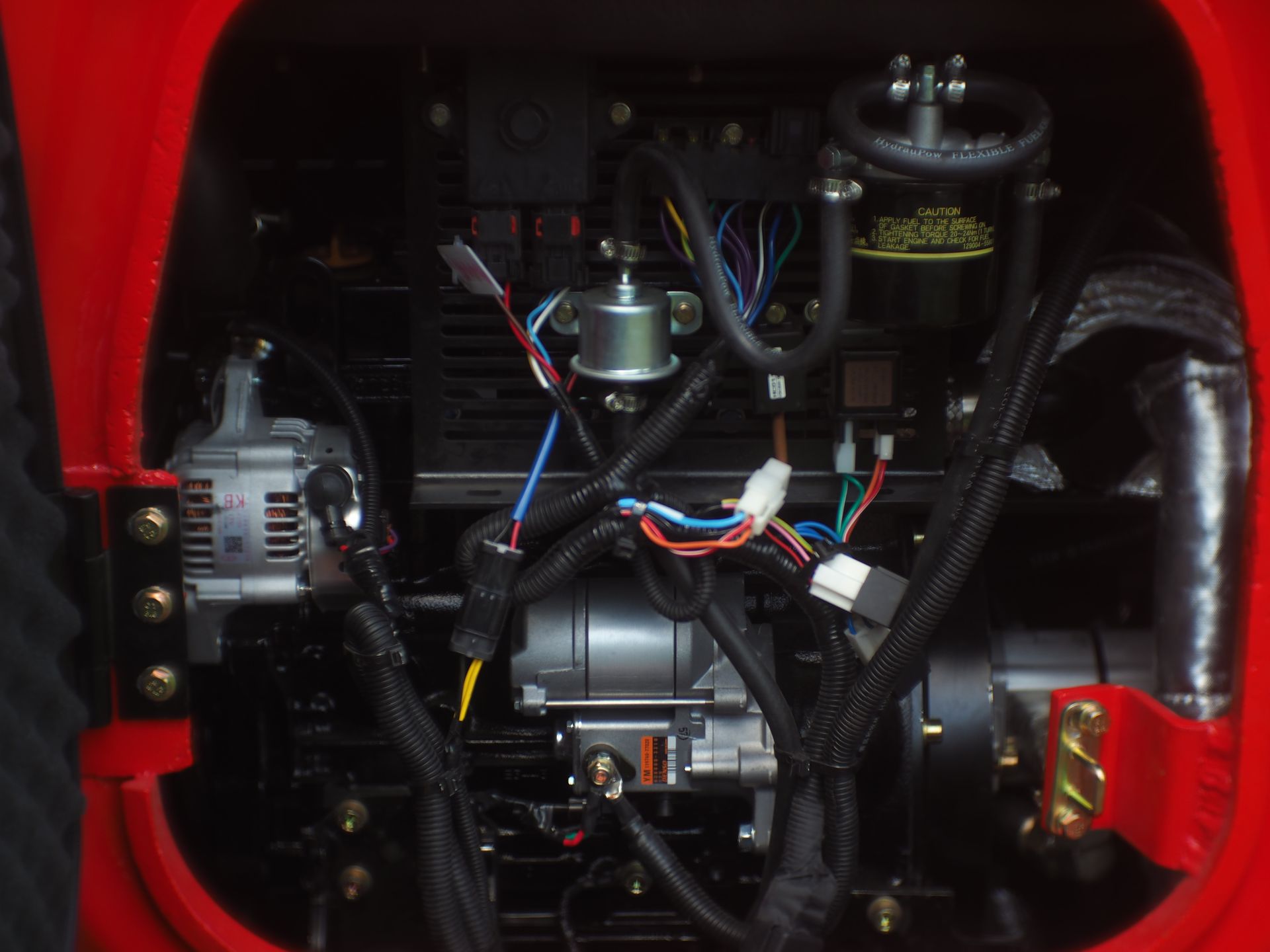 Red tractor engine compartment filled with wires, hoses, and components.