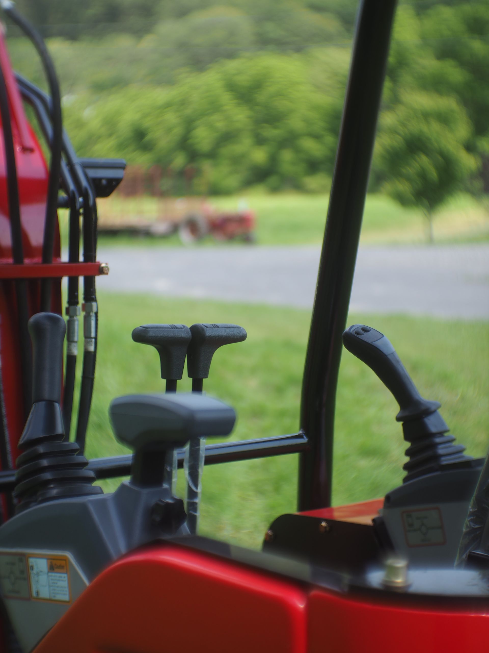 Red excavator control panel with joysticks and hand rests, green grass in background.
