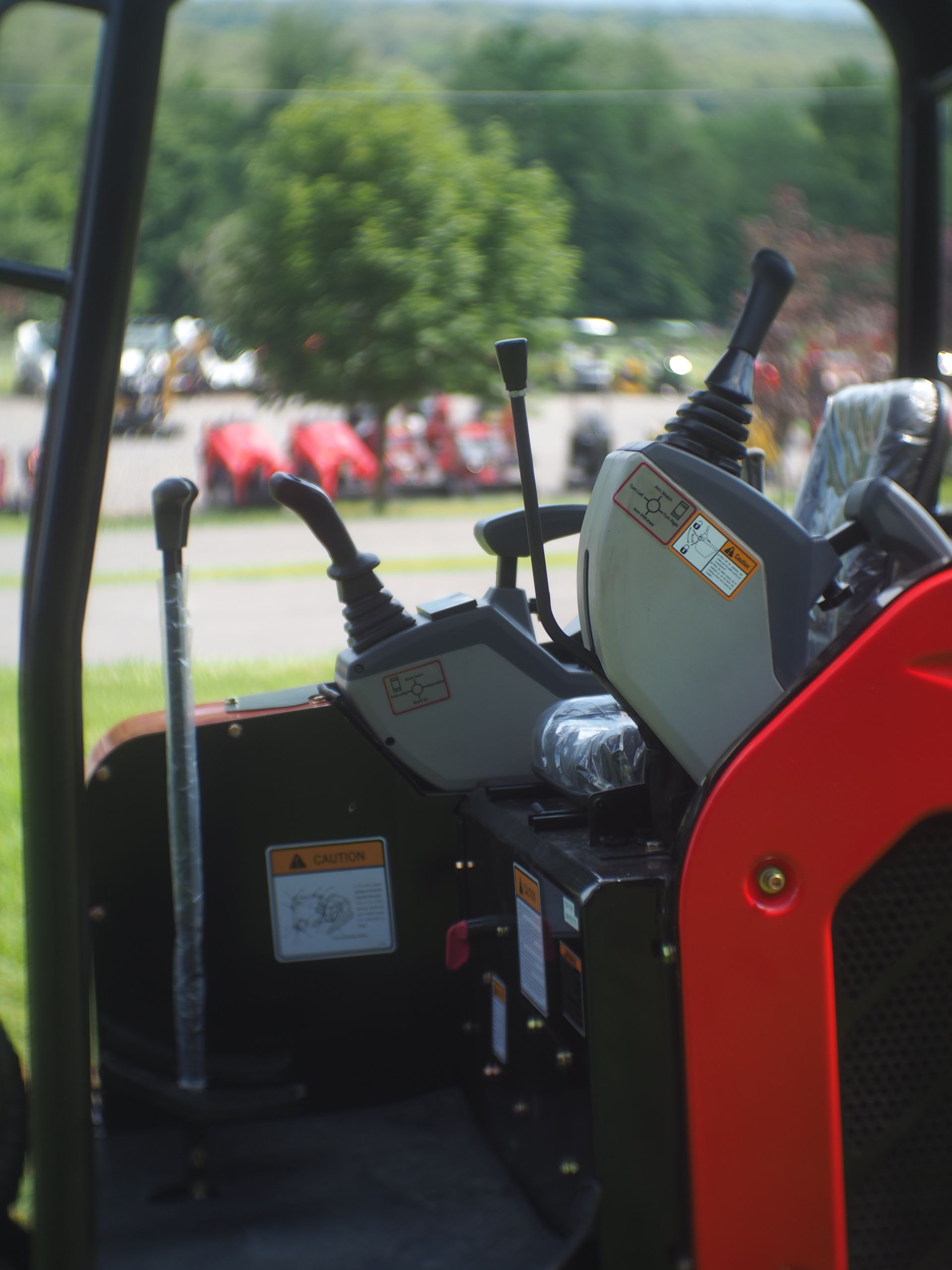 Interior view of an excavator. Levers, red frame, and warning labels are visible.