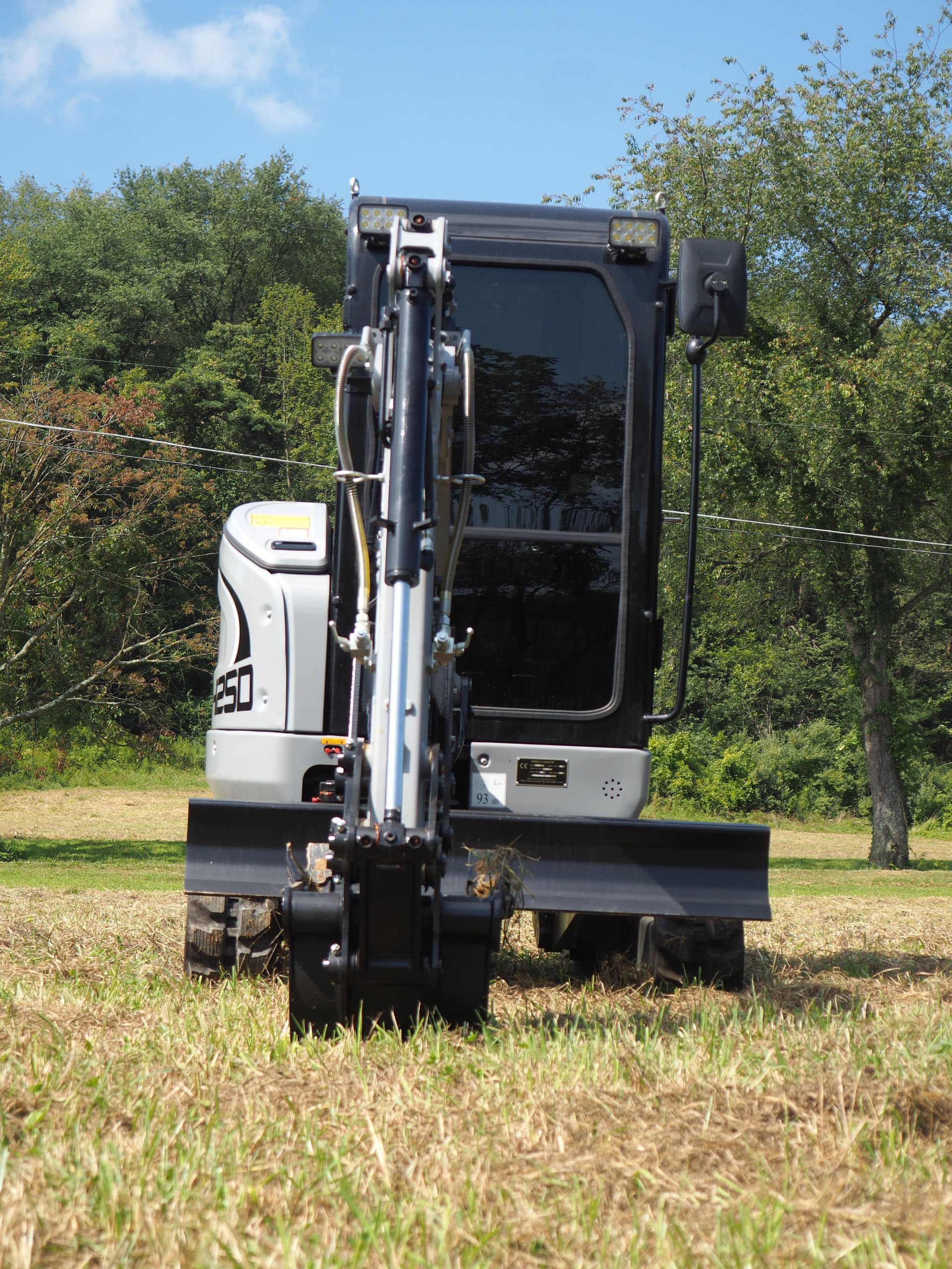 Mini excavator, black and gray, in a grassy field on a sunny day.