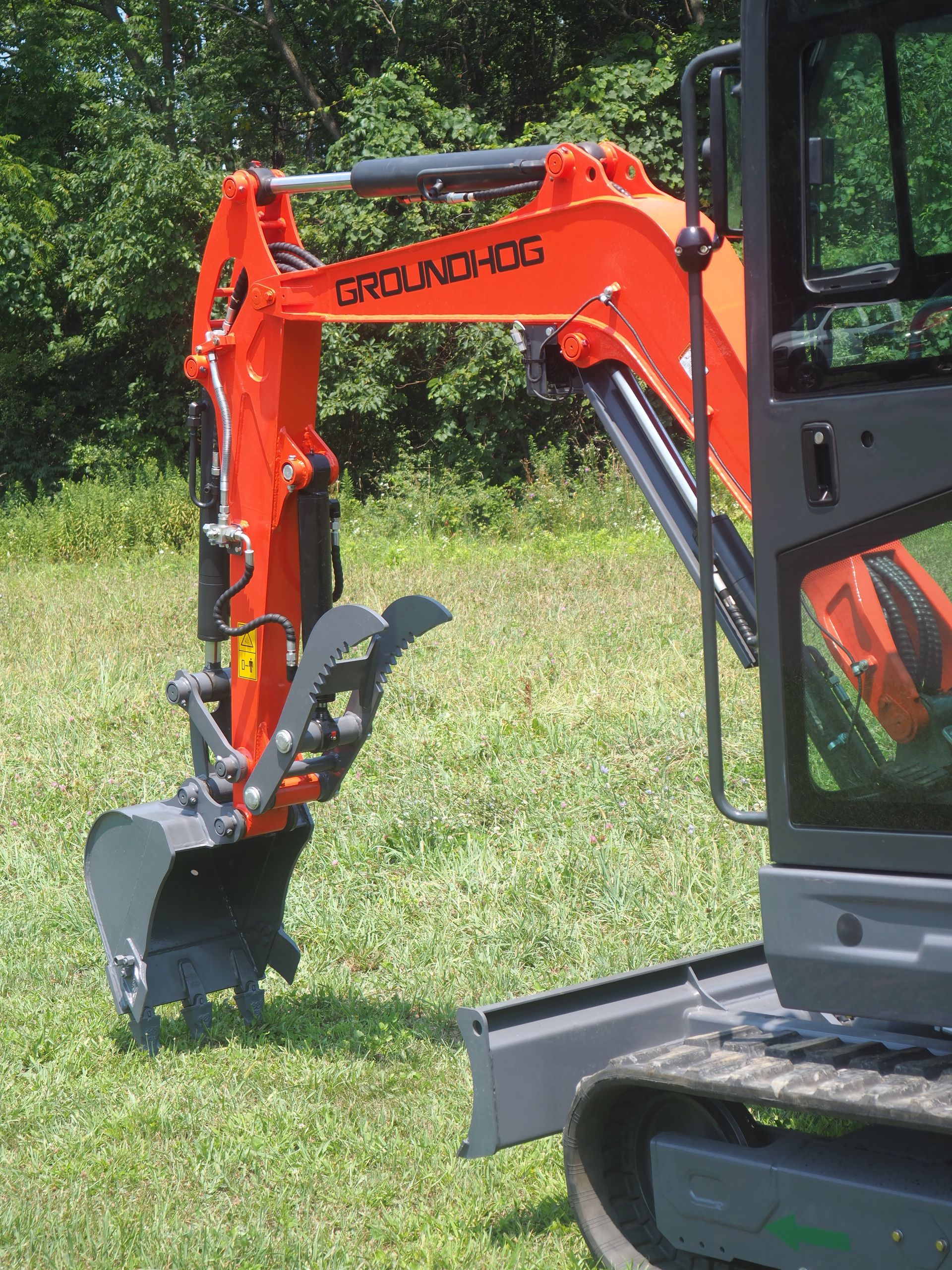 Orange Groundhog excavator arm, bucket resting on grass.