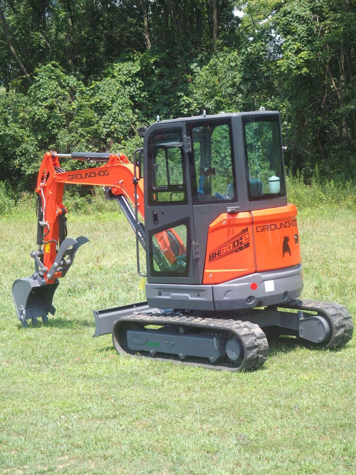 Orange and black Kubota mini excavator on grass, with trees in the background.