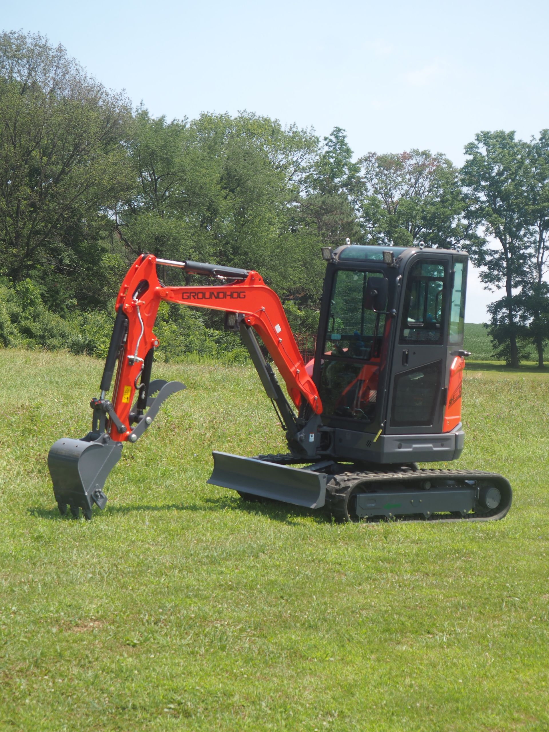 Orange and gray Kubota excavator on grass, trees in background.