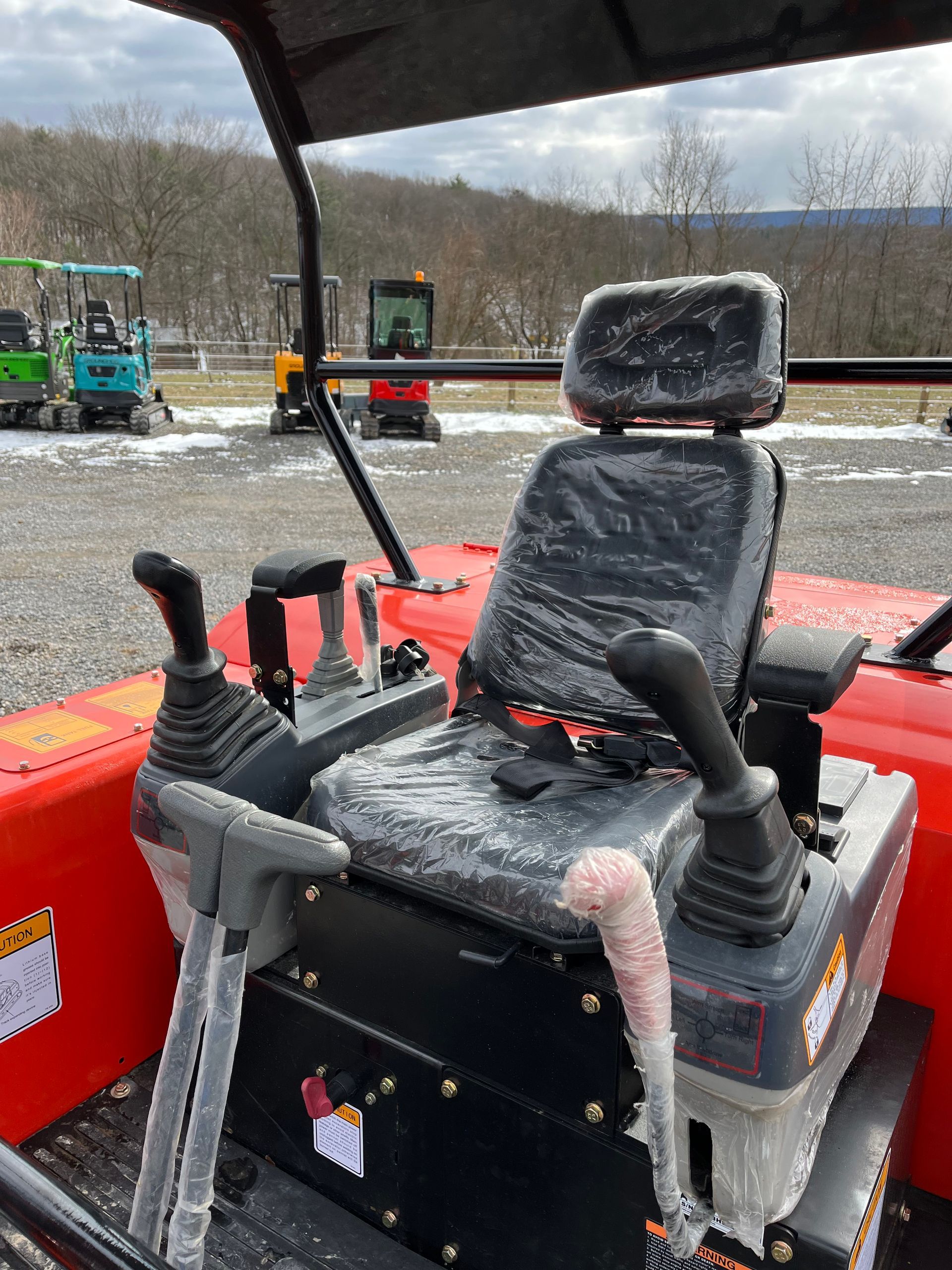 Interior view of a red excavator with controls, seat, and partially visible machinery in a yard.