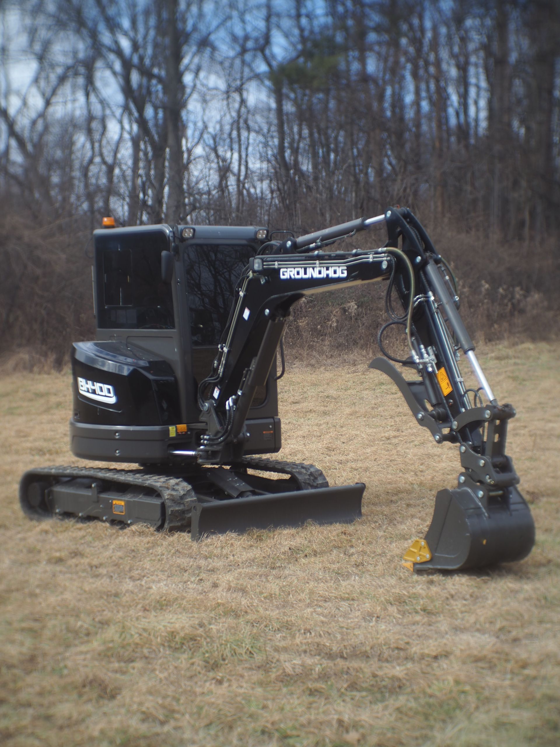 Black compact excavator on brown grass, trees in the background.