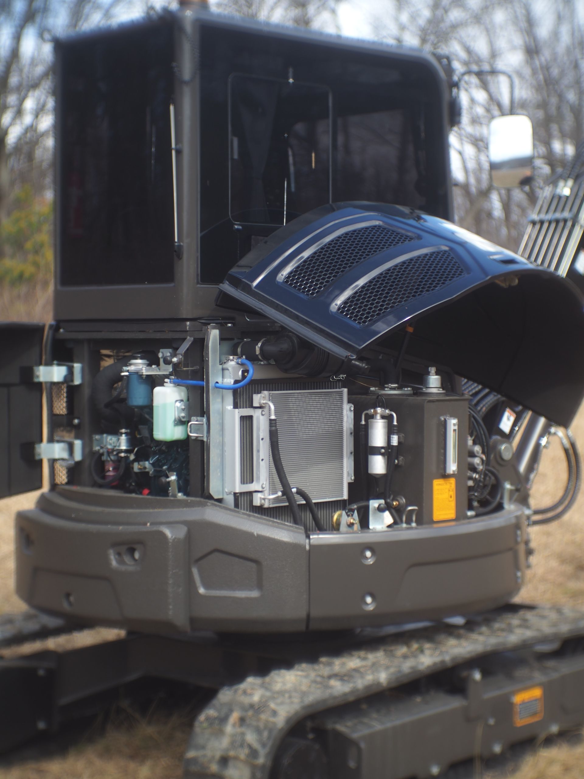 Dark gray excavator with hood and side panels open, revealing engine components.