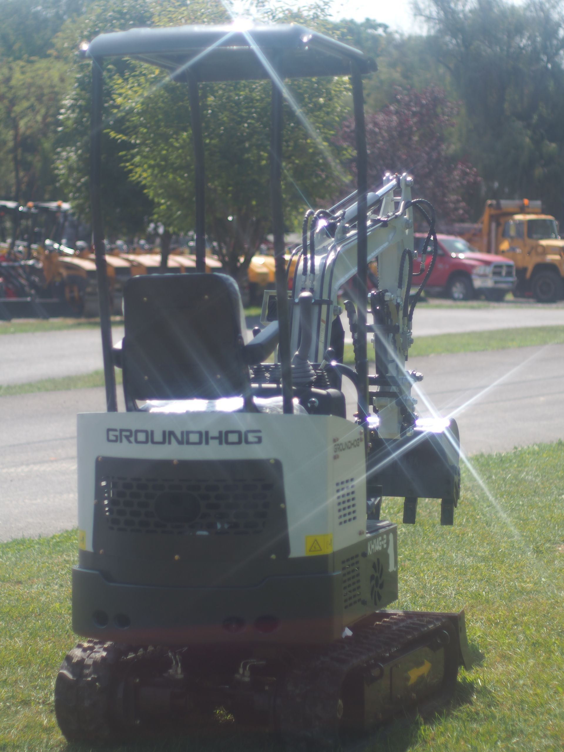 A small, white and black Groundhog excavator with a black roll cage, outdoors.