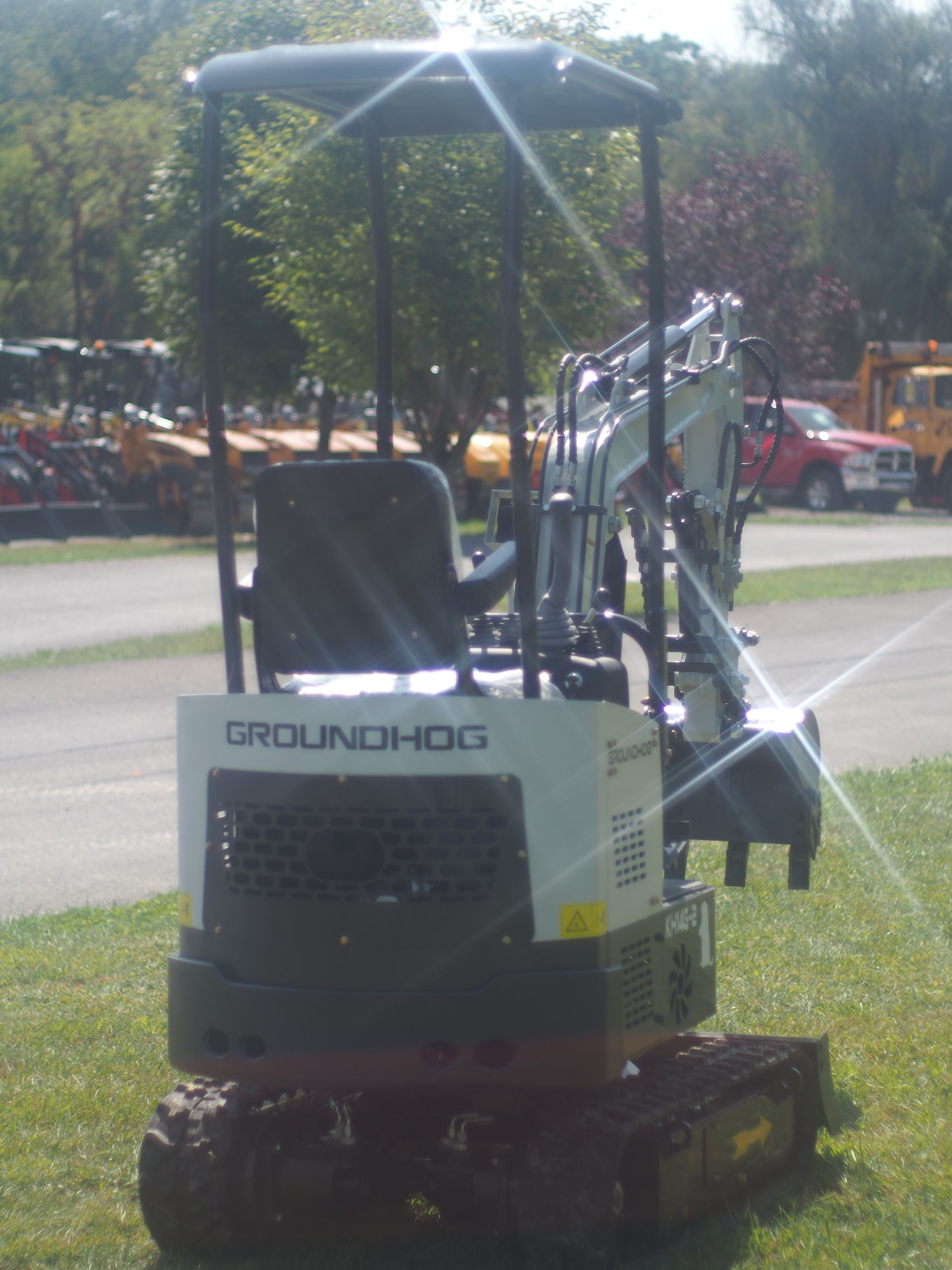 Mini excavator, Groundhog brand, on grass, outdoors with trees and a red pickup truck in background.