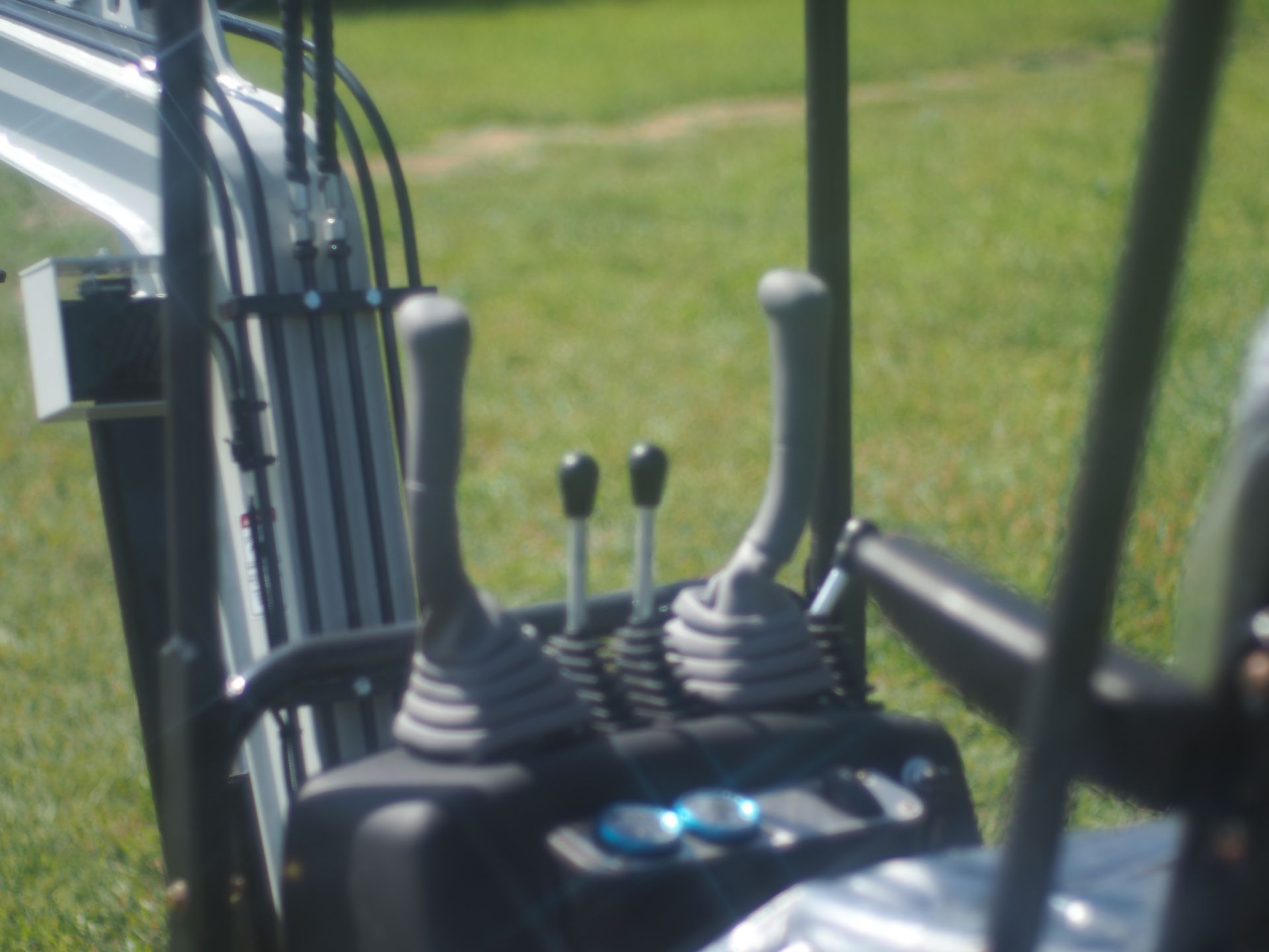 Close-up of an excavator's control panel with two joysticks and other levers in a grassy field.