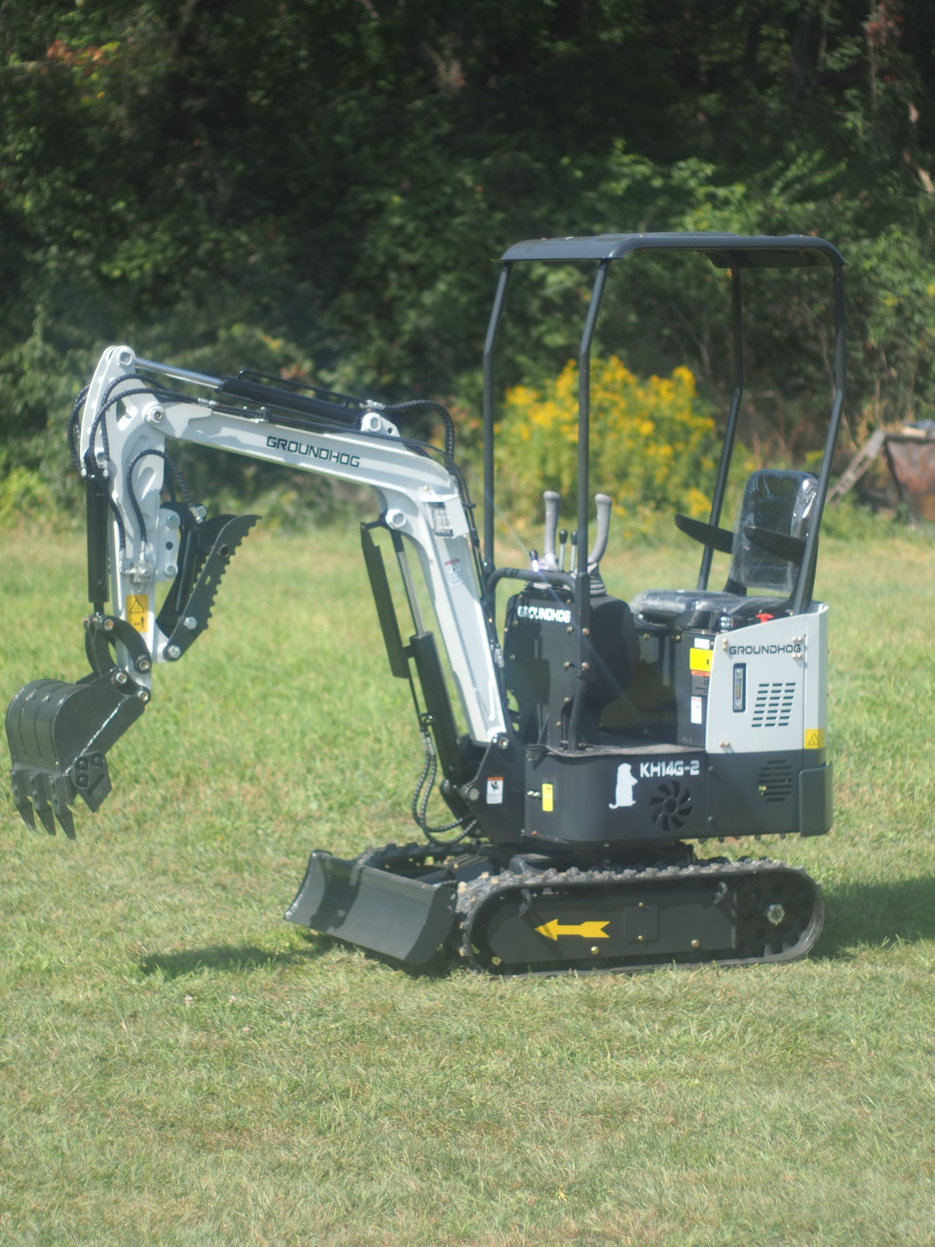 Mini excavator on grass, with black and silver arm extended, sunlight.
