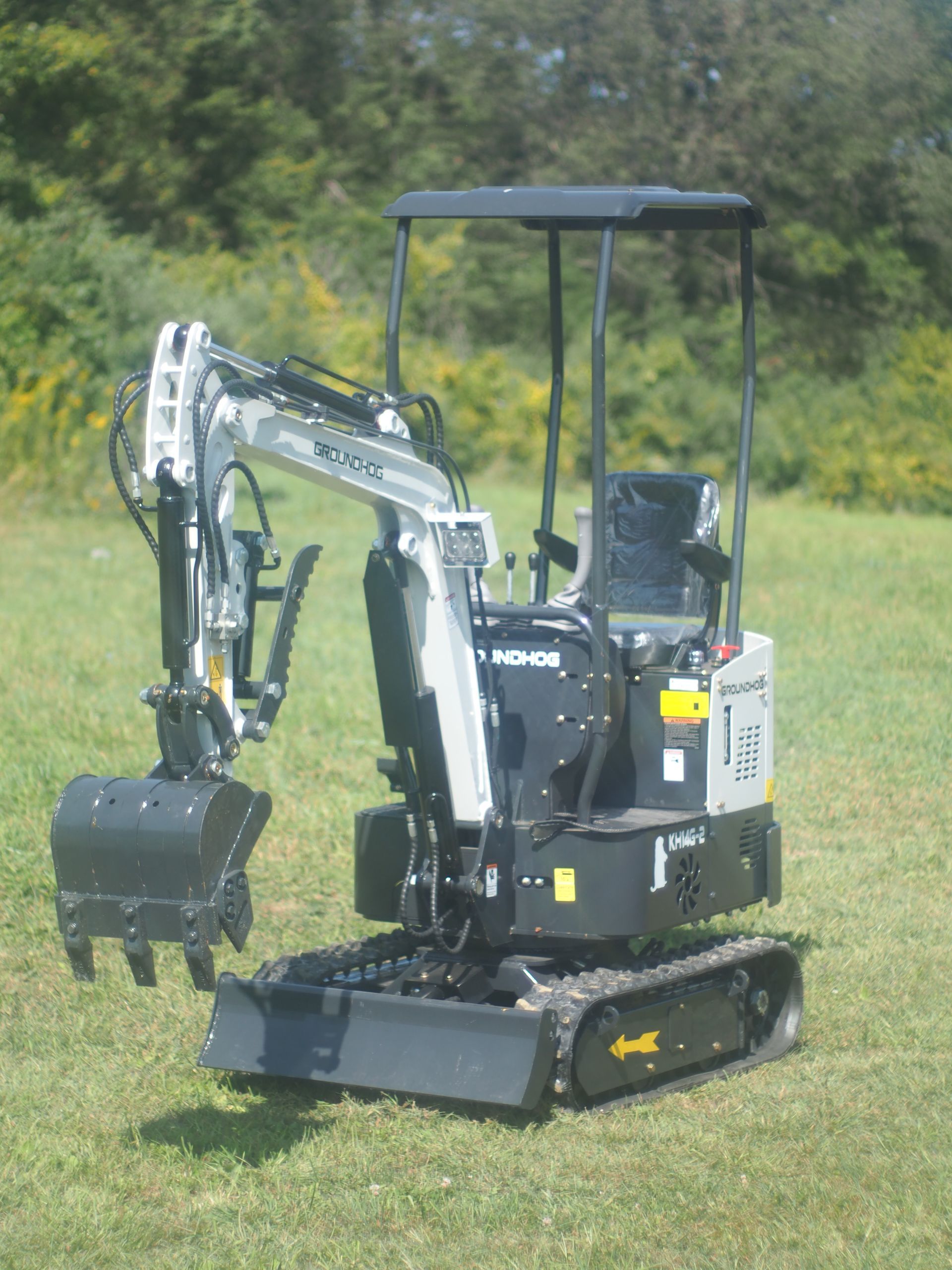 Small, gray and black excavator on grass, with bucket and treads extended.