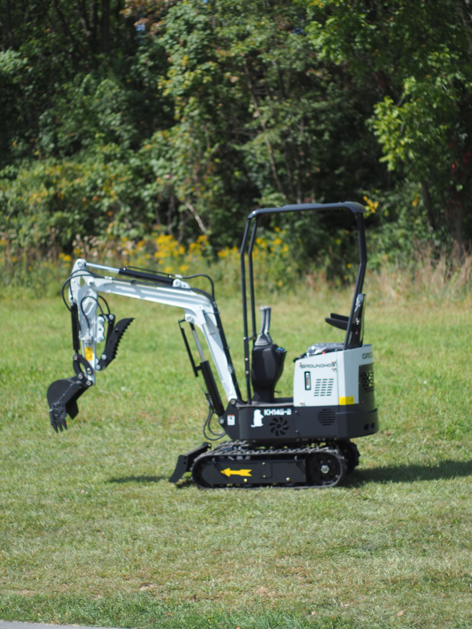 Mini excavator on a grassy lawn, arm extended, with trees in the background.