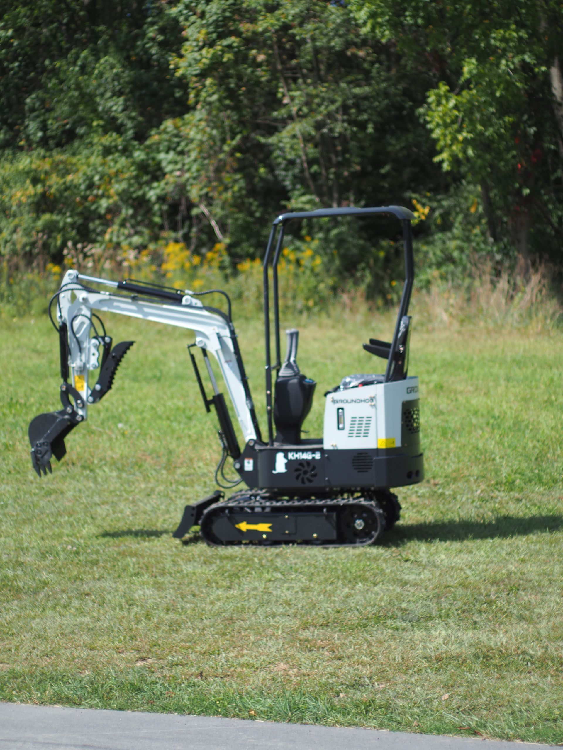 Mini excavator on grass with trees in the background.