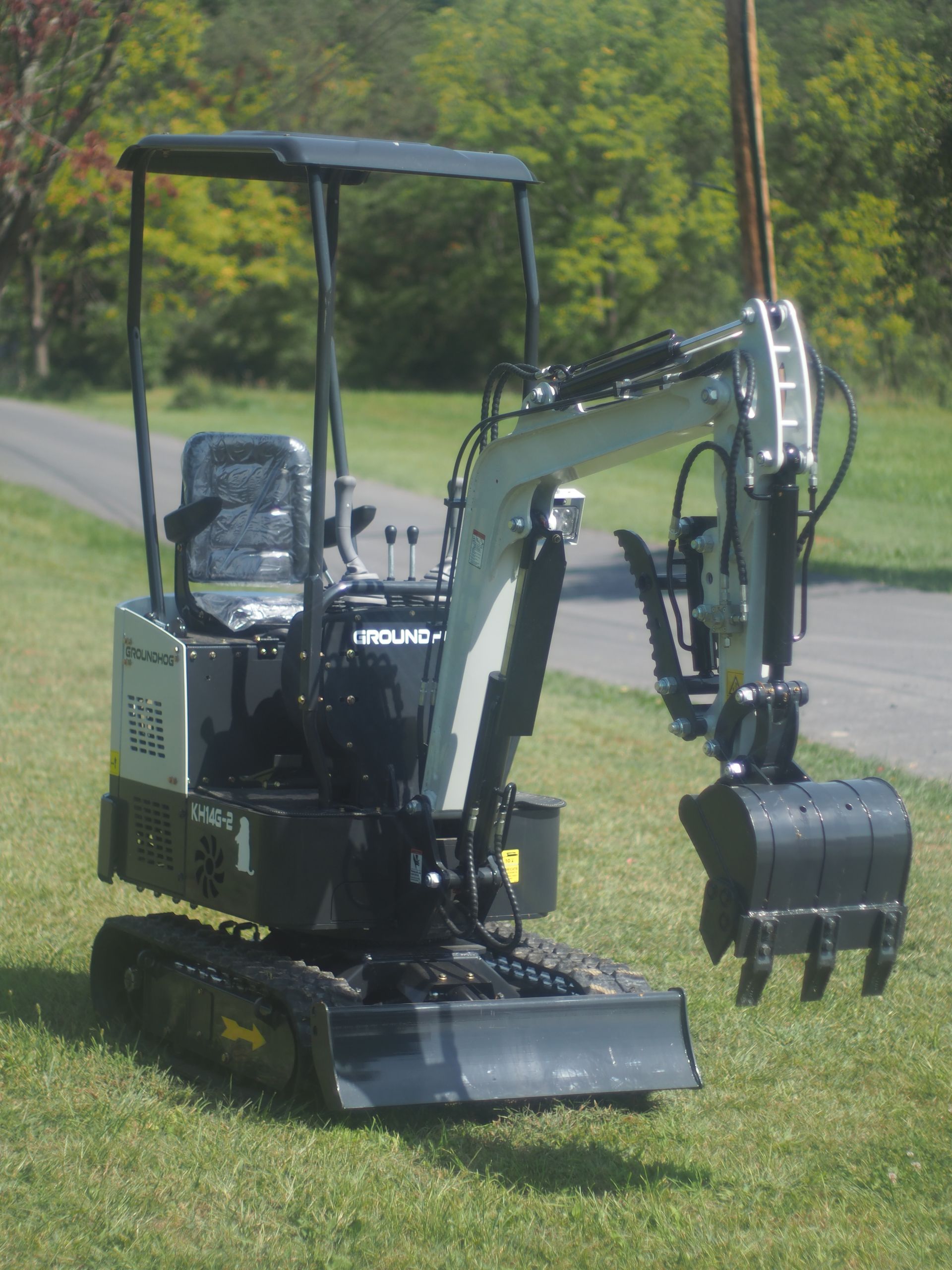A small, silver and black excavator on a grassy lawn next to a paved road, with a bucket extended.
