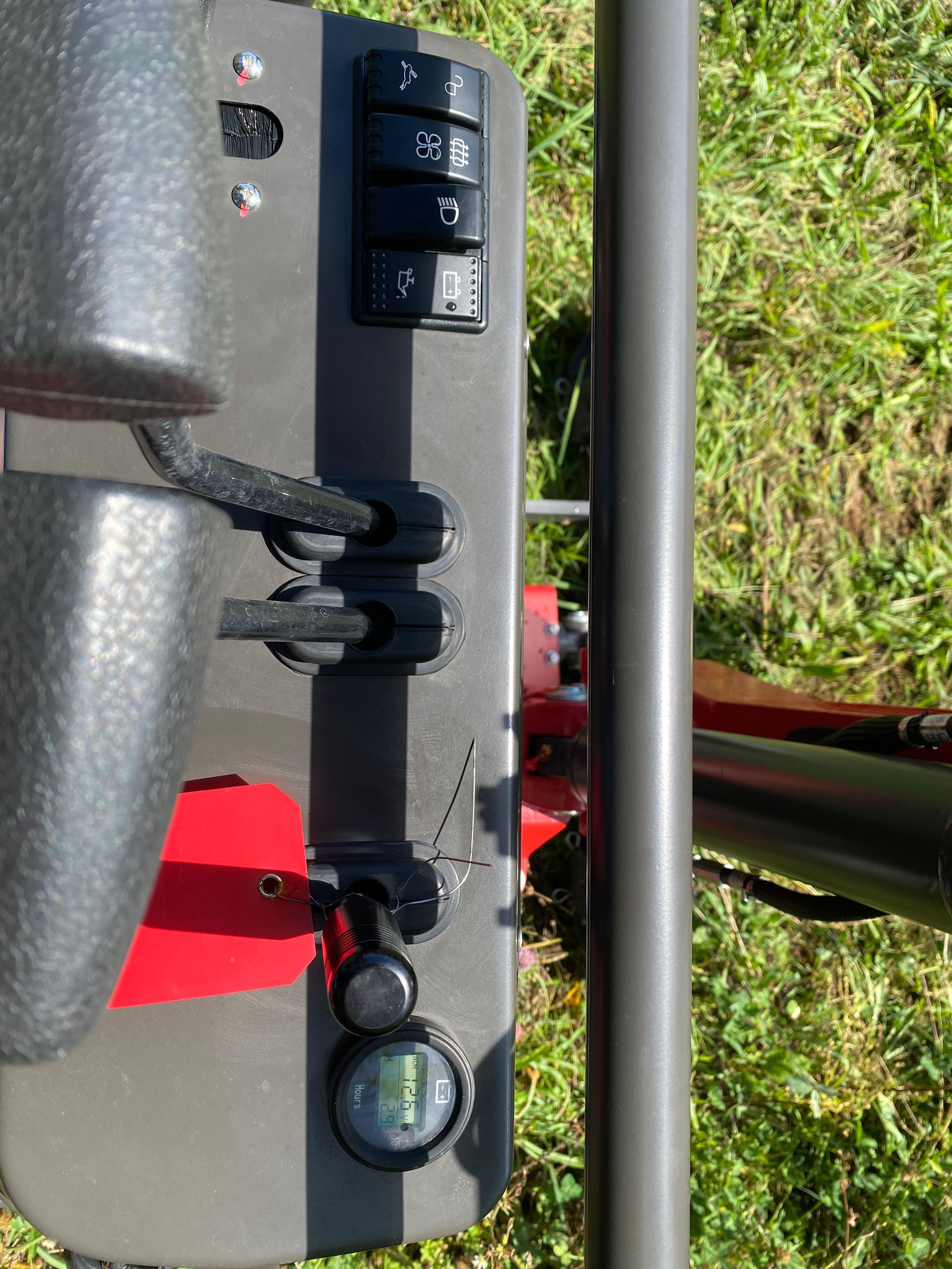 Close-up of a device with control buttons, black arm, and a bubble level against a grassy background.