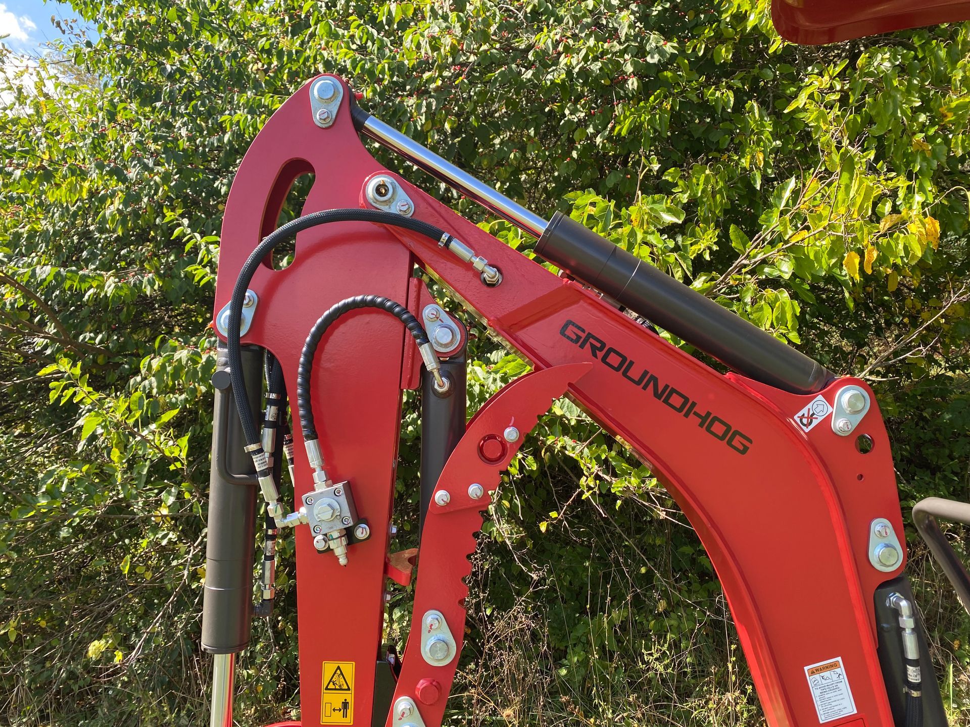 Red Groundhog backhoe arm with hydraulic cylinders and hoses, outdoors.