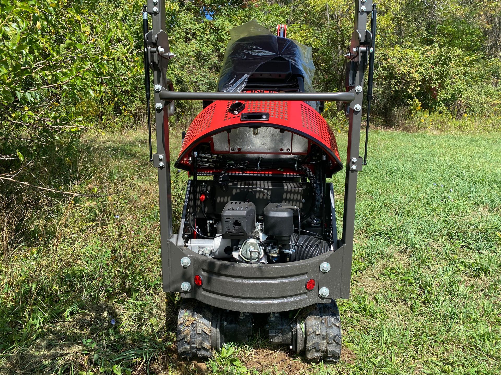 Rear view of a small red and grey tractor-like machine with tracks in a grassy field.