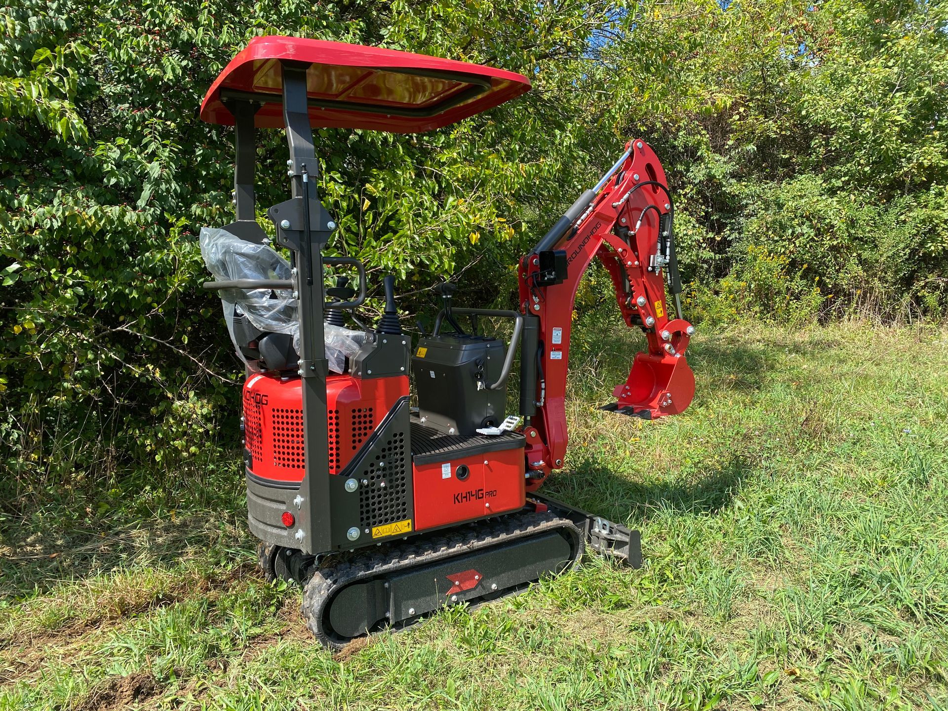 Red mini excavator on a grassy hill, operating outdoors.