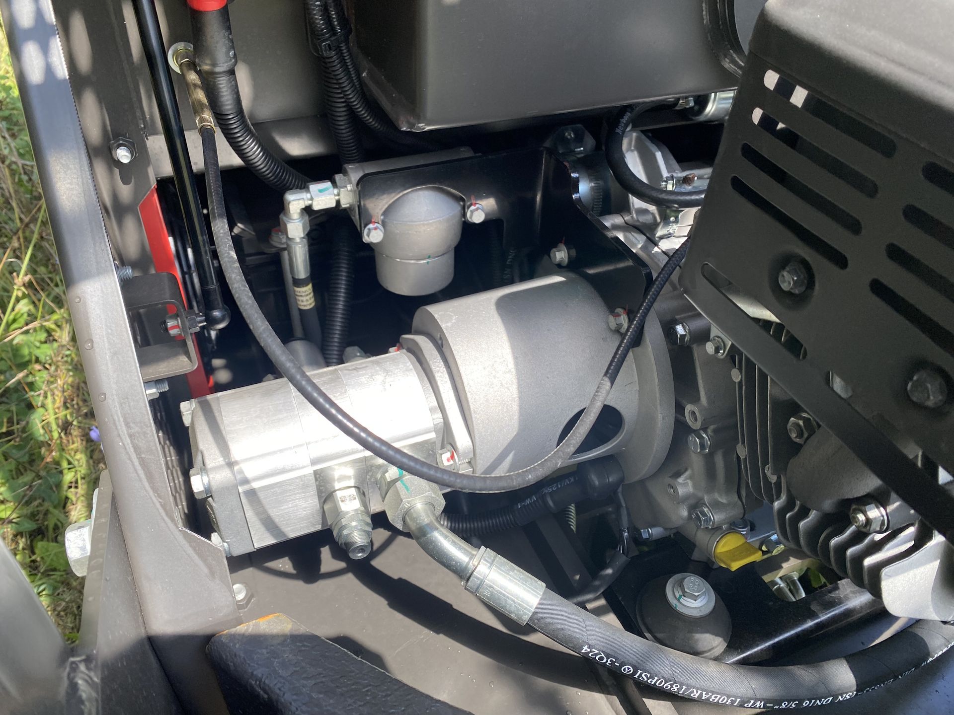 Engine compartment of a machine, featuring a cylindrical pump and various hoses and components.