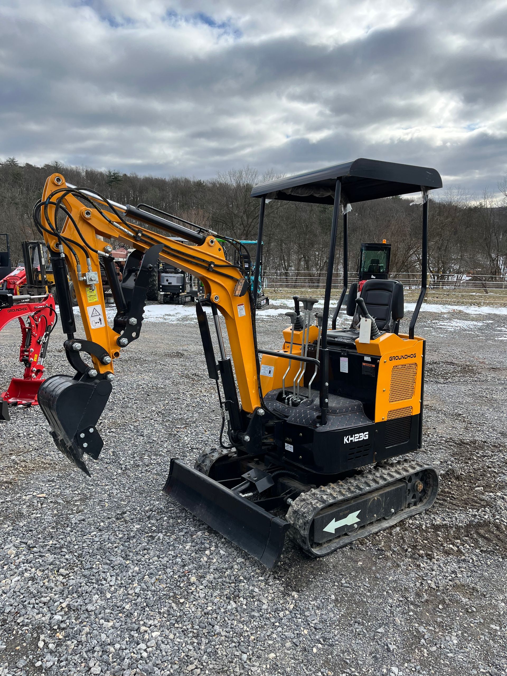 Yellow and black mini excavator on a gravel surface with a snowy background.
