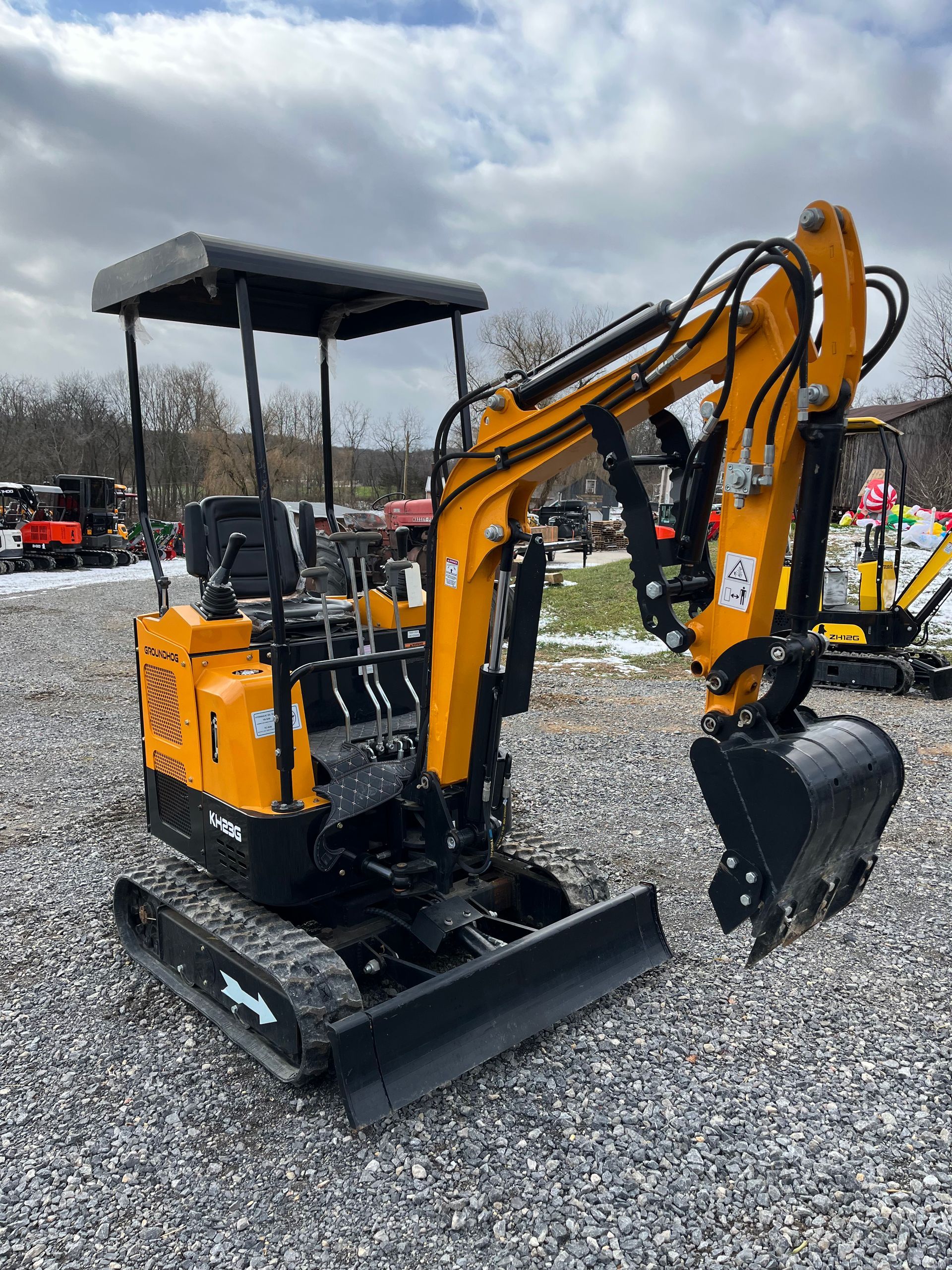 Yellow and black mini excavator on a gravel lot under an overcast sky.
