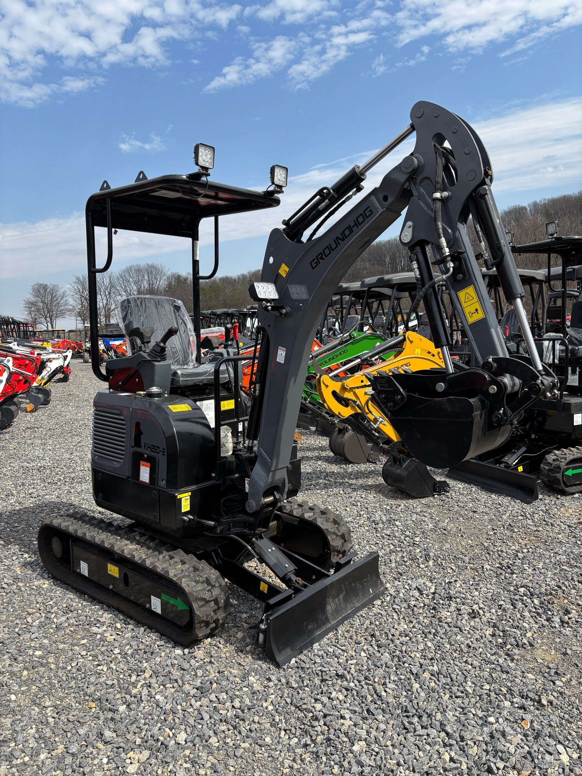 A small, black excavator on a gravel lot under a blue sky.