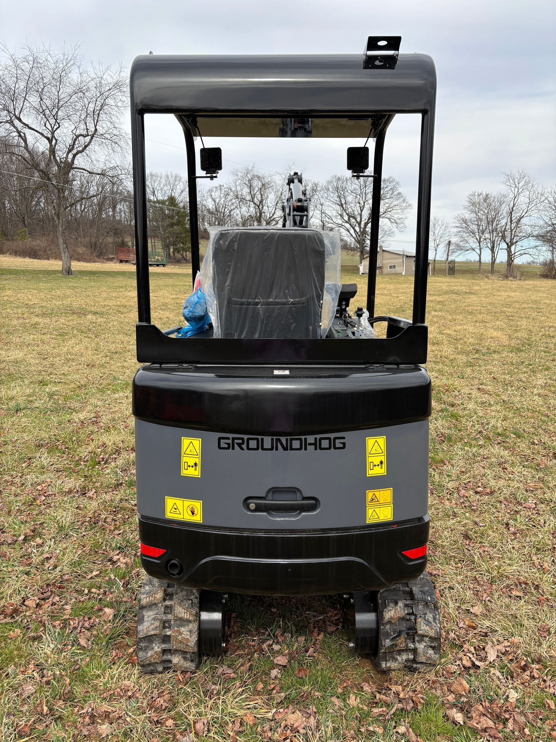 Gray and black Groundhog mini excavator on a grassy field, with a roll bar.