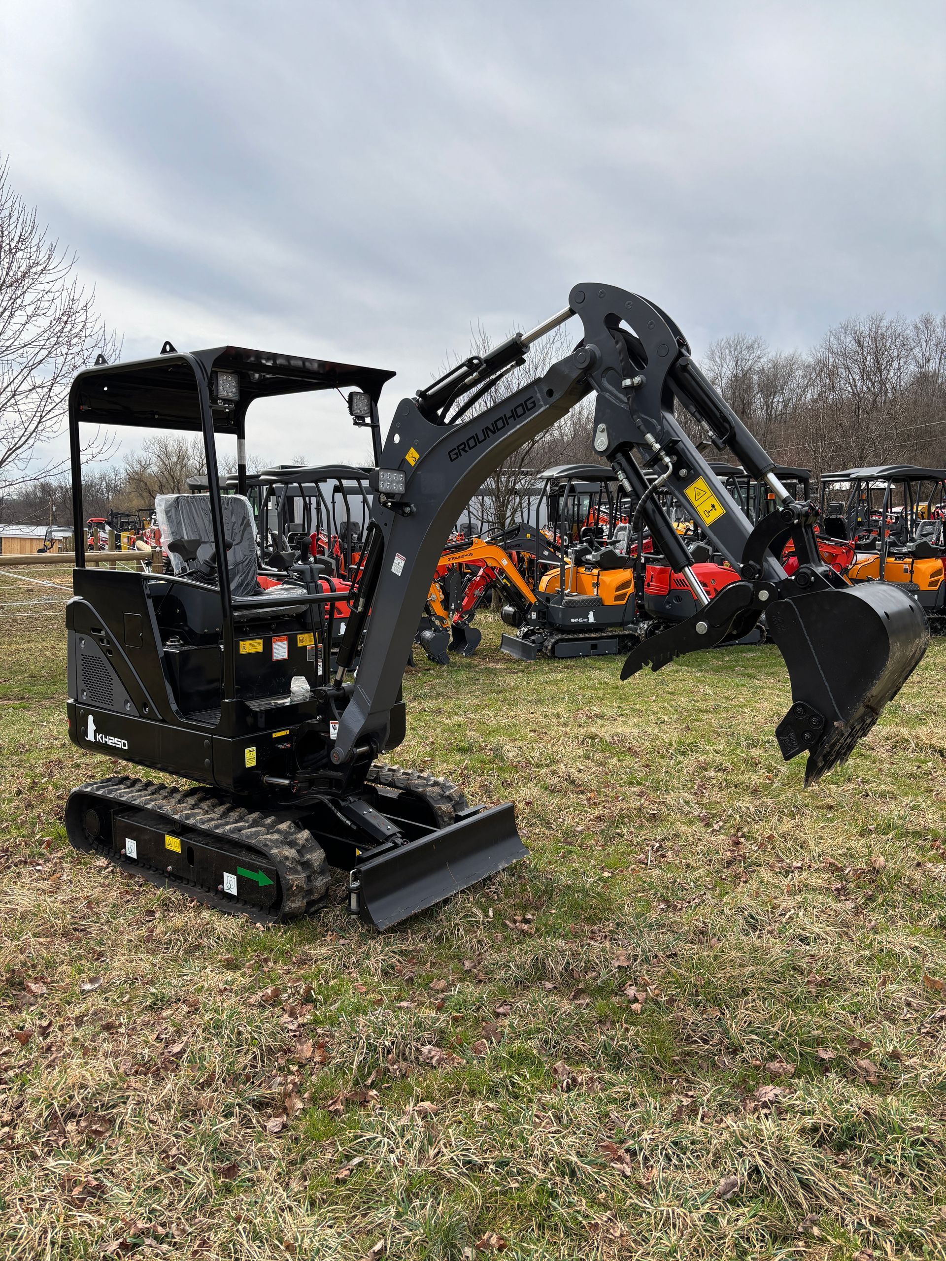 Black mini excavator on a grassy field with other construction equipment in the background.