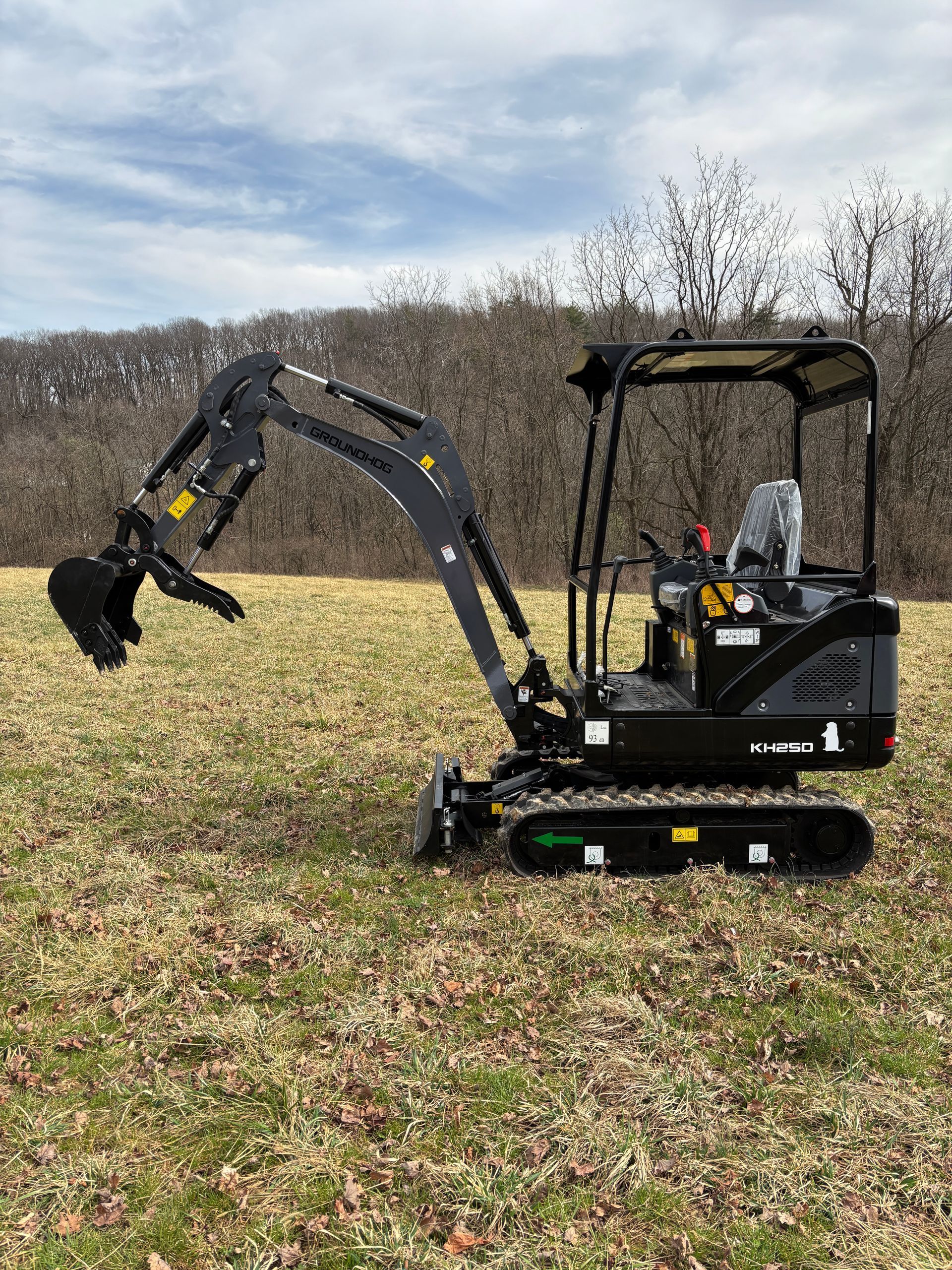 Black mini excavator in a grassy field, ready to dig.