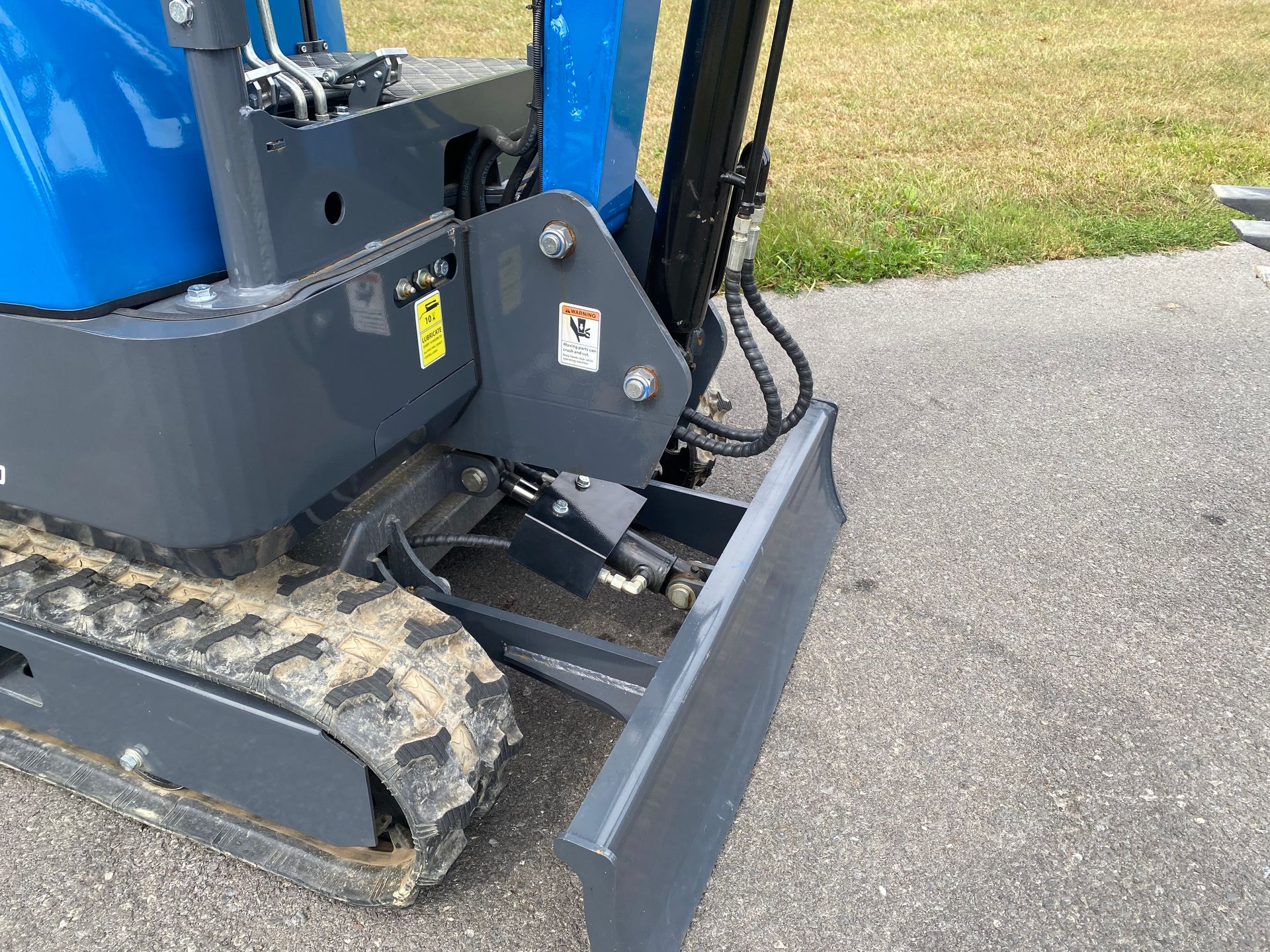 Mini excavator, blue and gray, with tracks and a blade, outdoors on pavement.