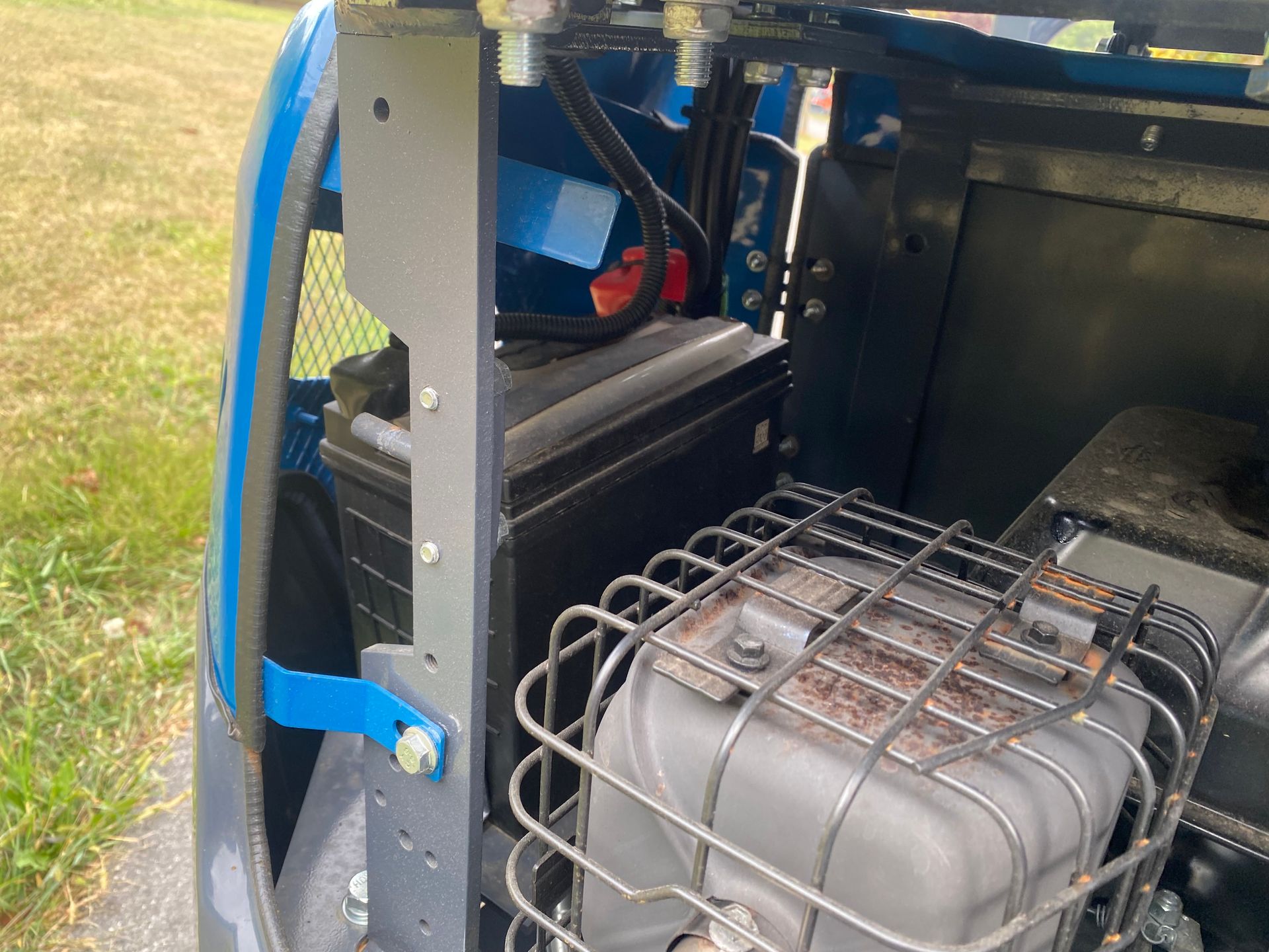 A black battery, wires, and a caged component inside a blue and gray machine.
