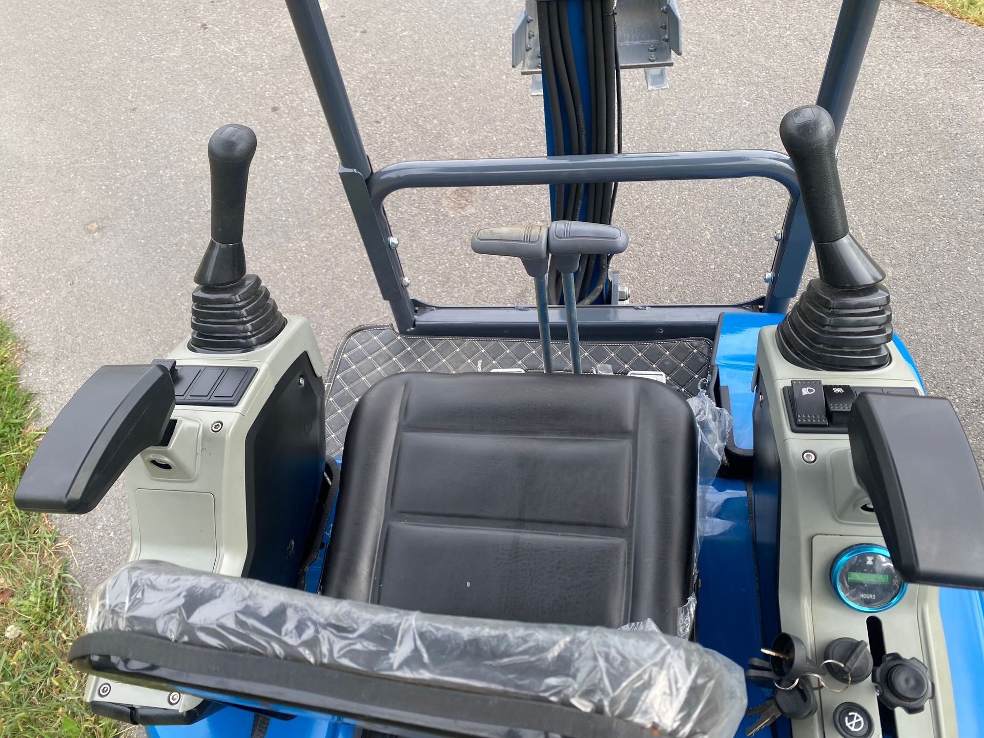 Close-up of mini excavator controls: black seat, joysticks, gauges, and blue and gray frame.