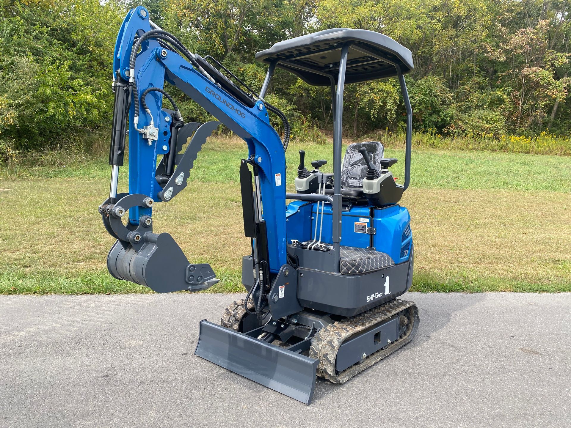Blue mini excavator on asphalt, bucket lowered, ready for work.
