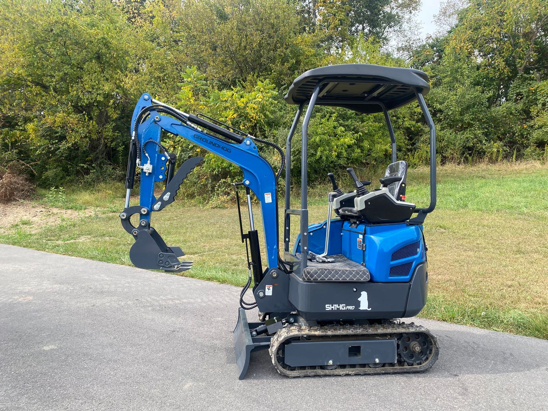 Blue mini excavator on a paved surface with a grassy background.