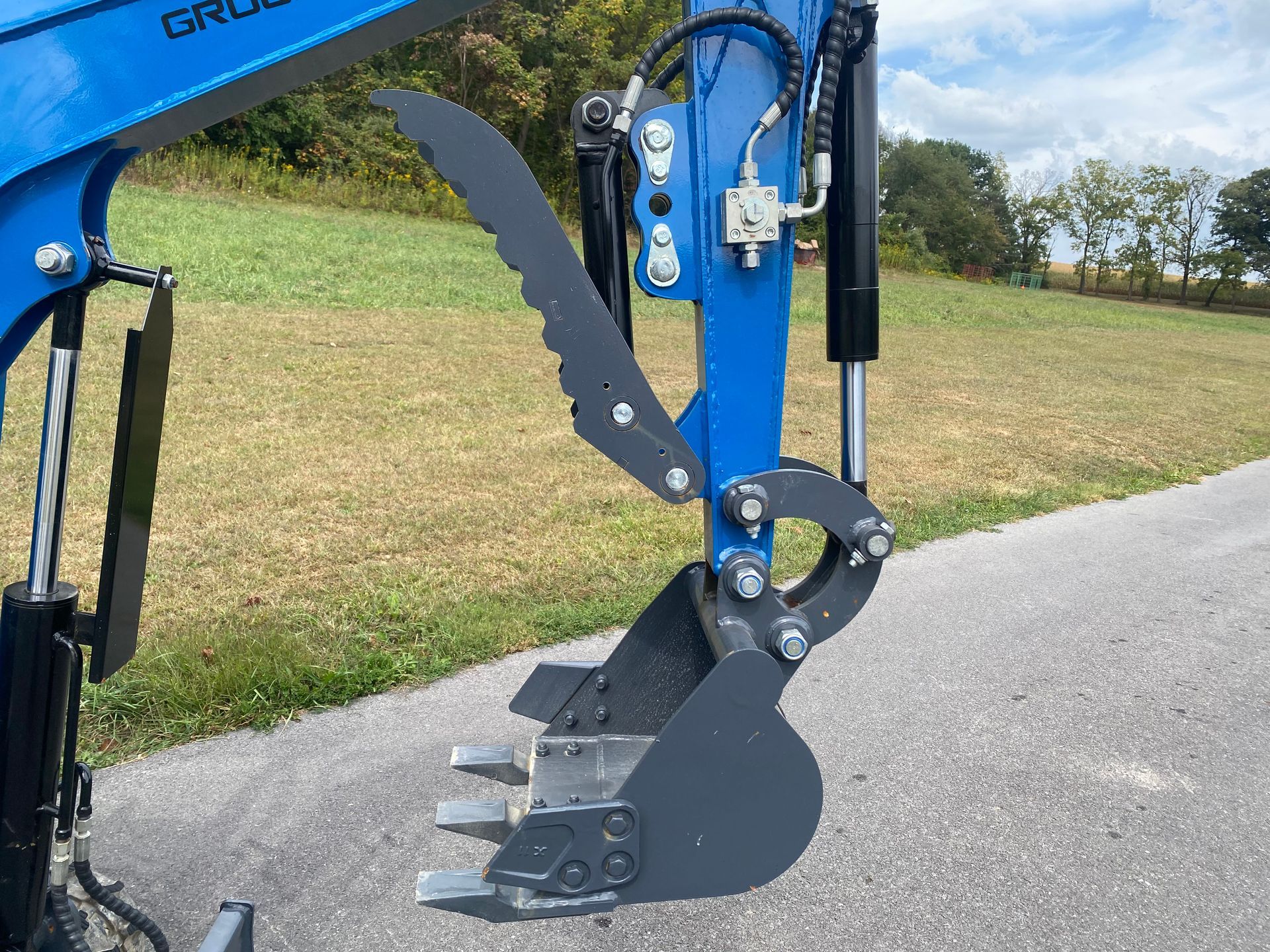 Blue and gray excavator bucket with claw attachment on a gravel road.