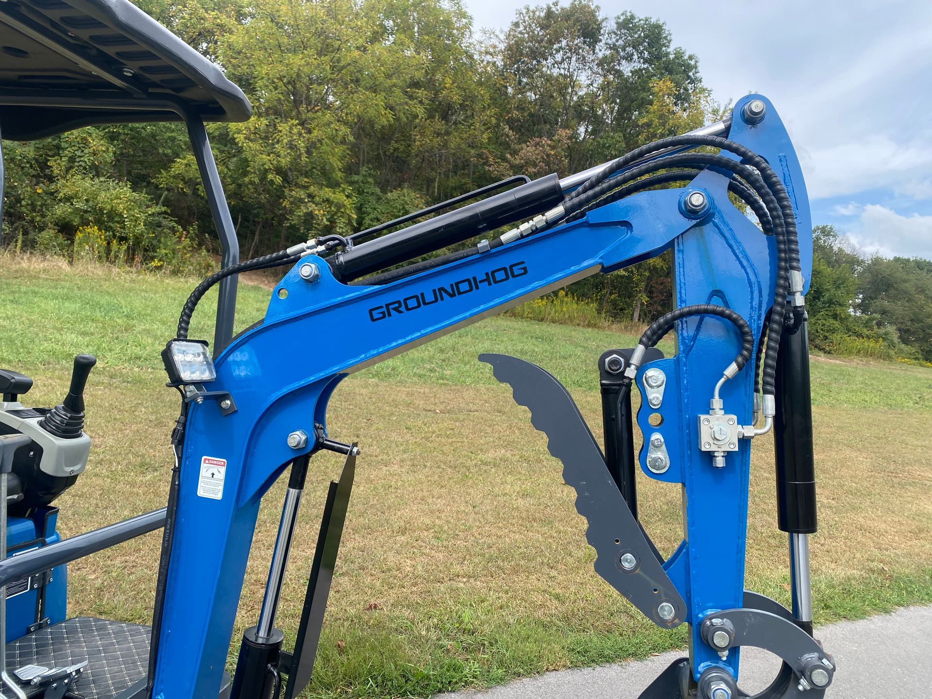 Blue mini excavator arm with hydraulic cylinders, outdoors.