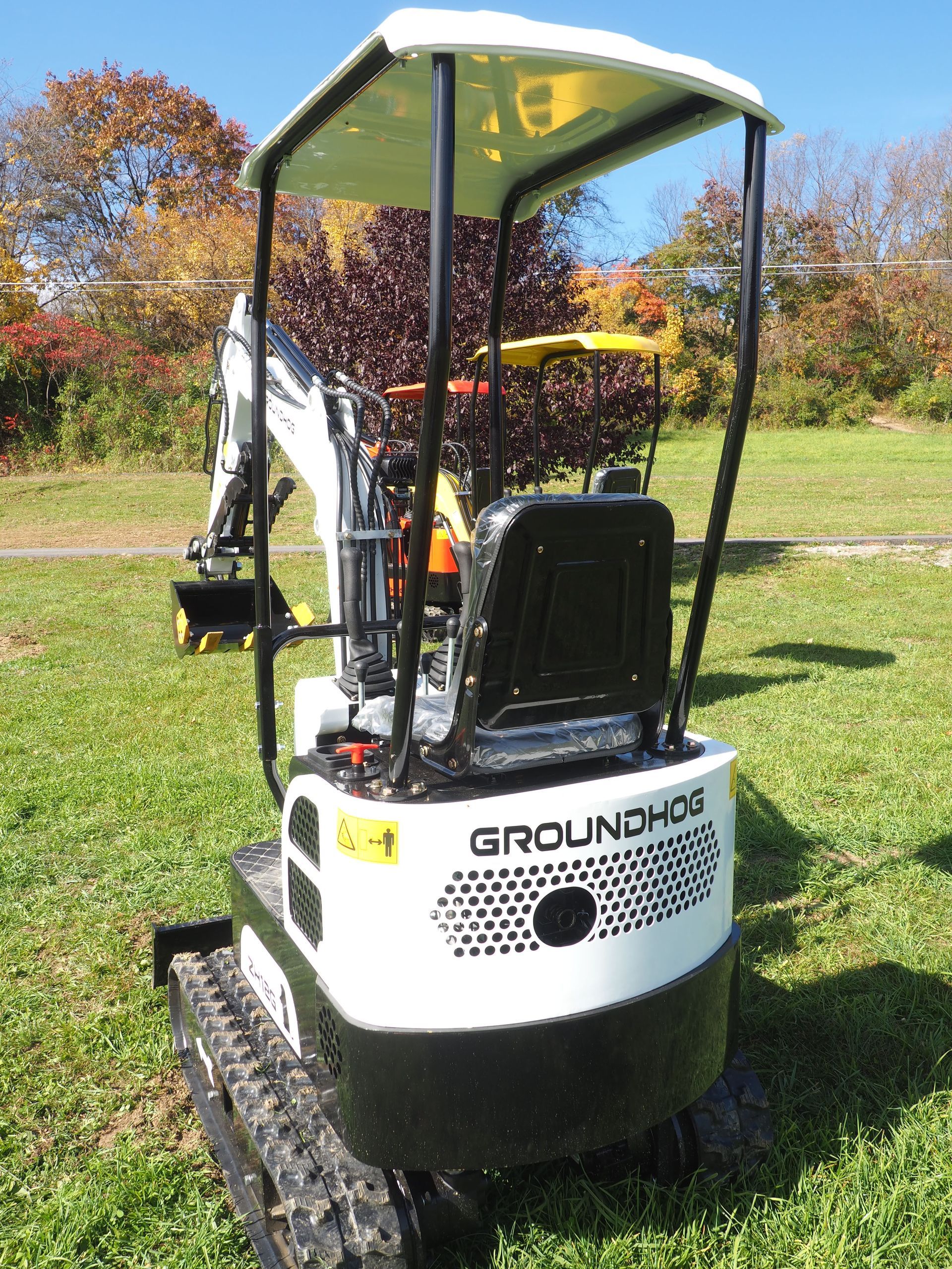 White and black mini excavator with a yellow canopy, in a grassy area.