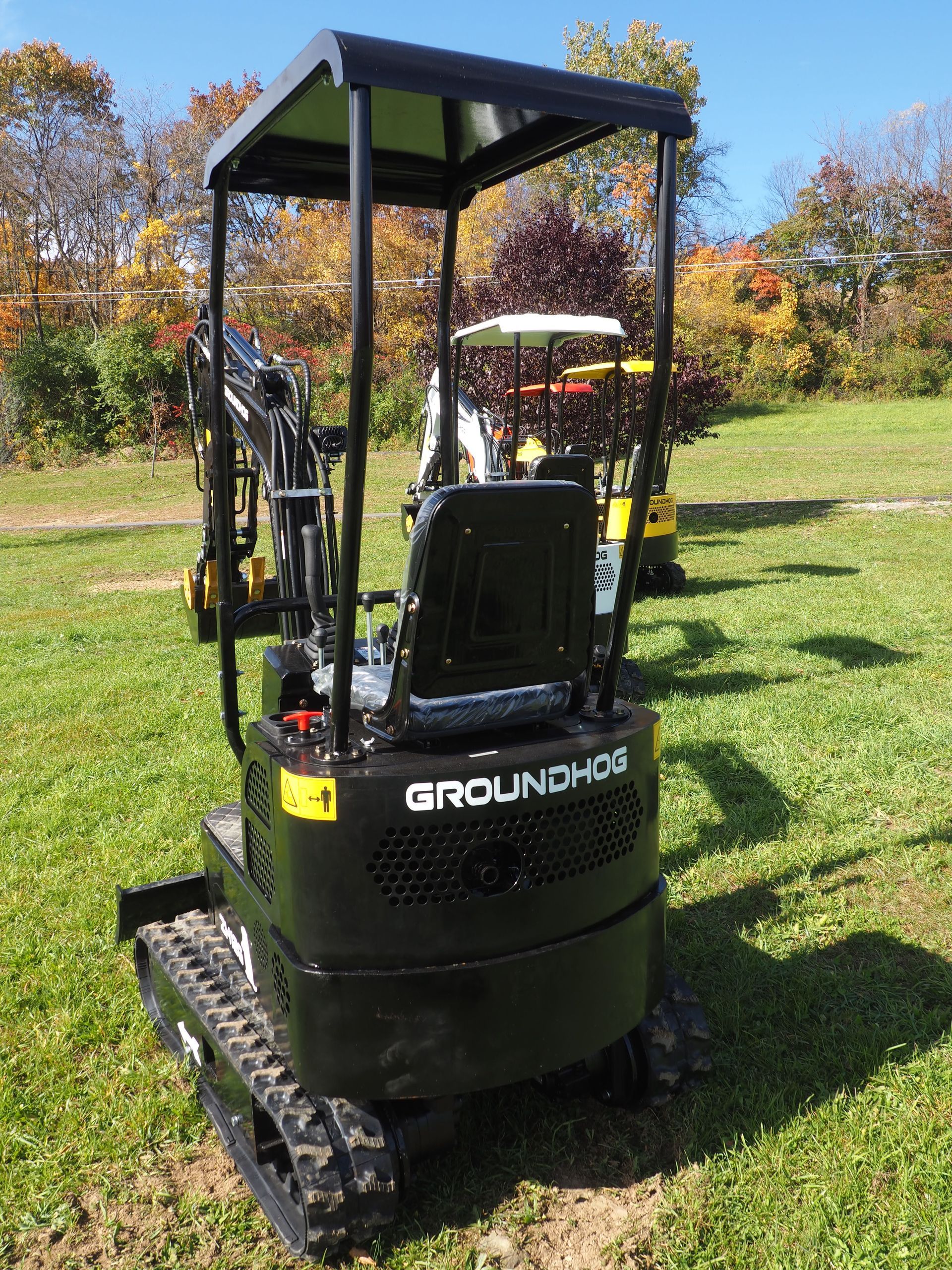 Black Groundhog mini excavator on grass with protective overhead frame.