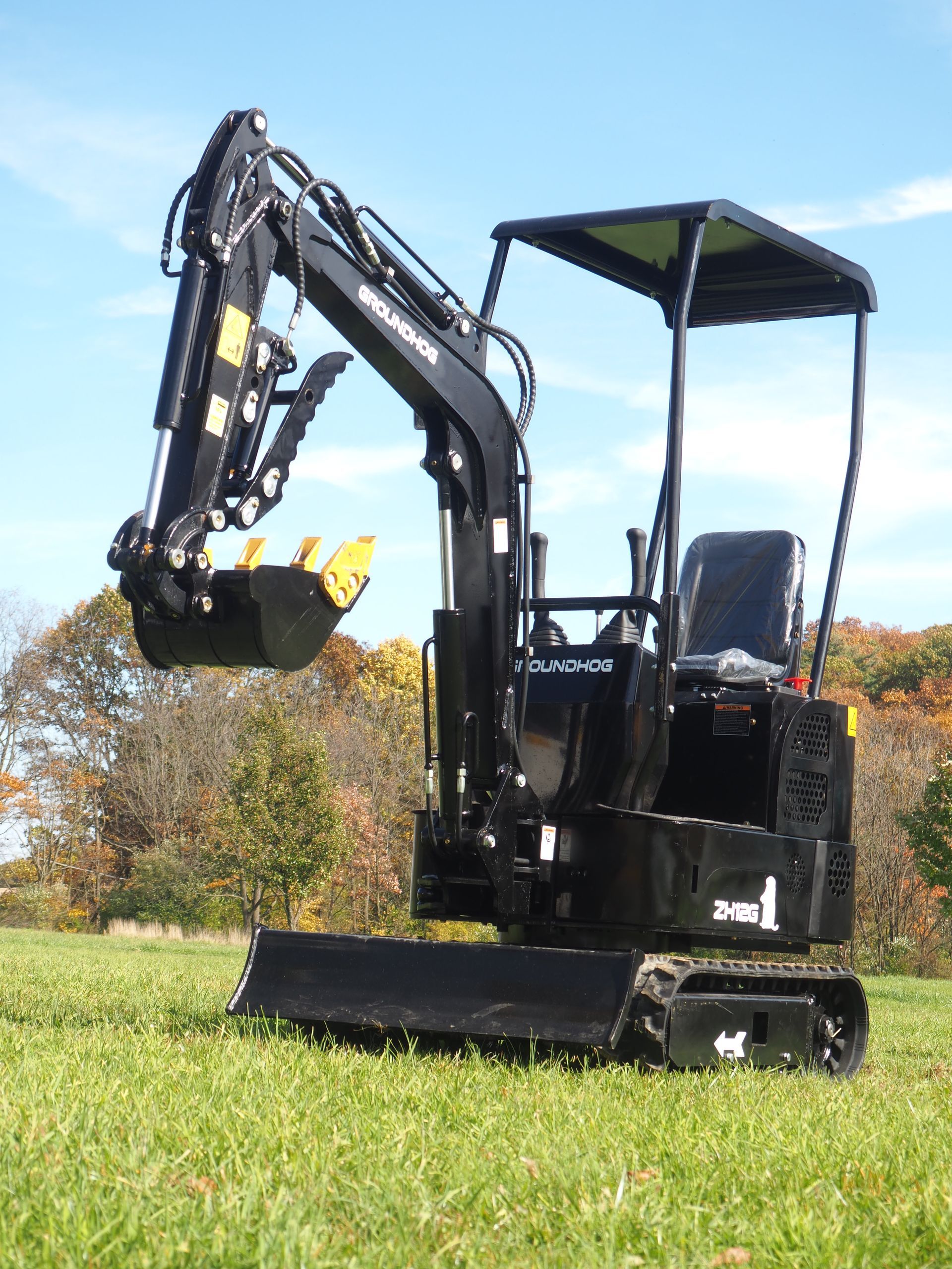 Black mini excavator on a grassy field. The boom arm is raised and the bucket is open.