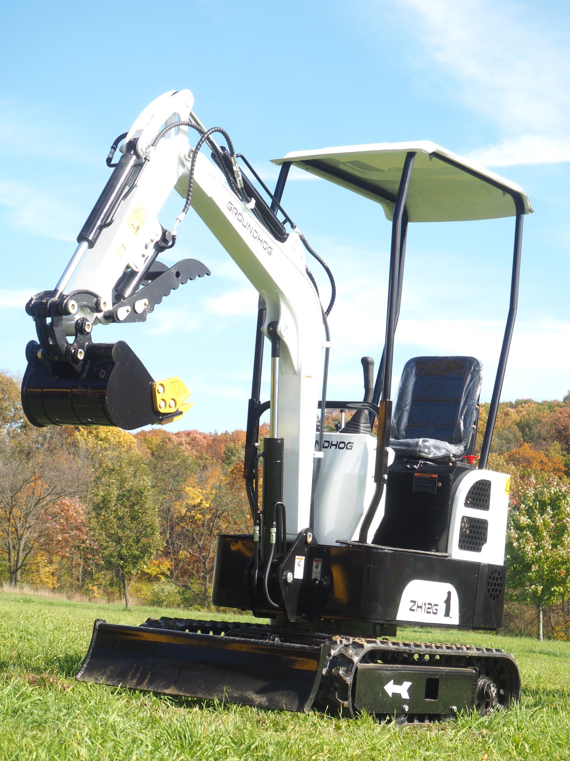 Small white and black excavator on tracks with a raised arm and bucket, outdoors on grass.