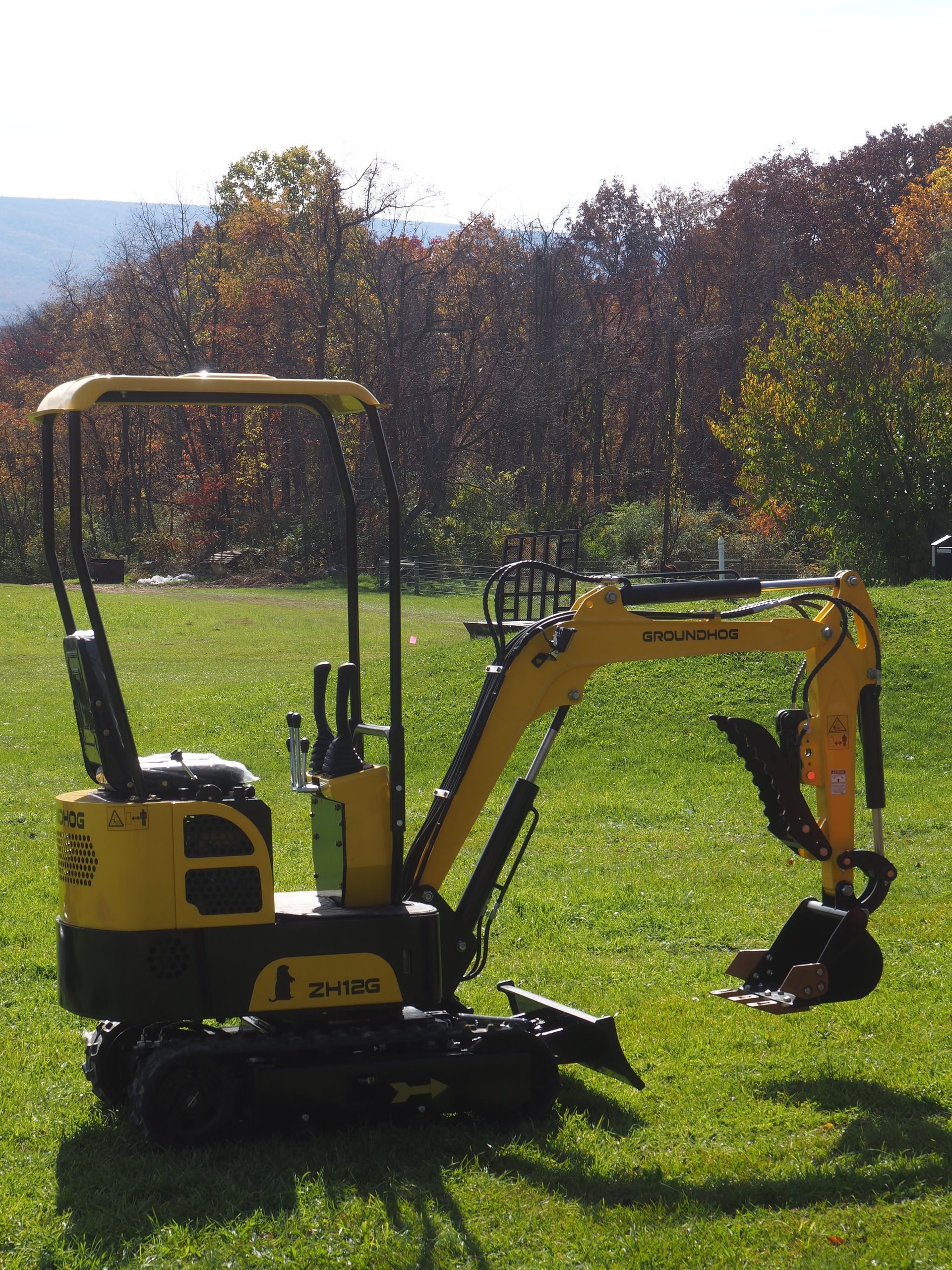 Yellow mini excavator on a grassy lawn with trees in the background, sunny day.