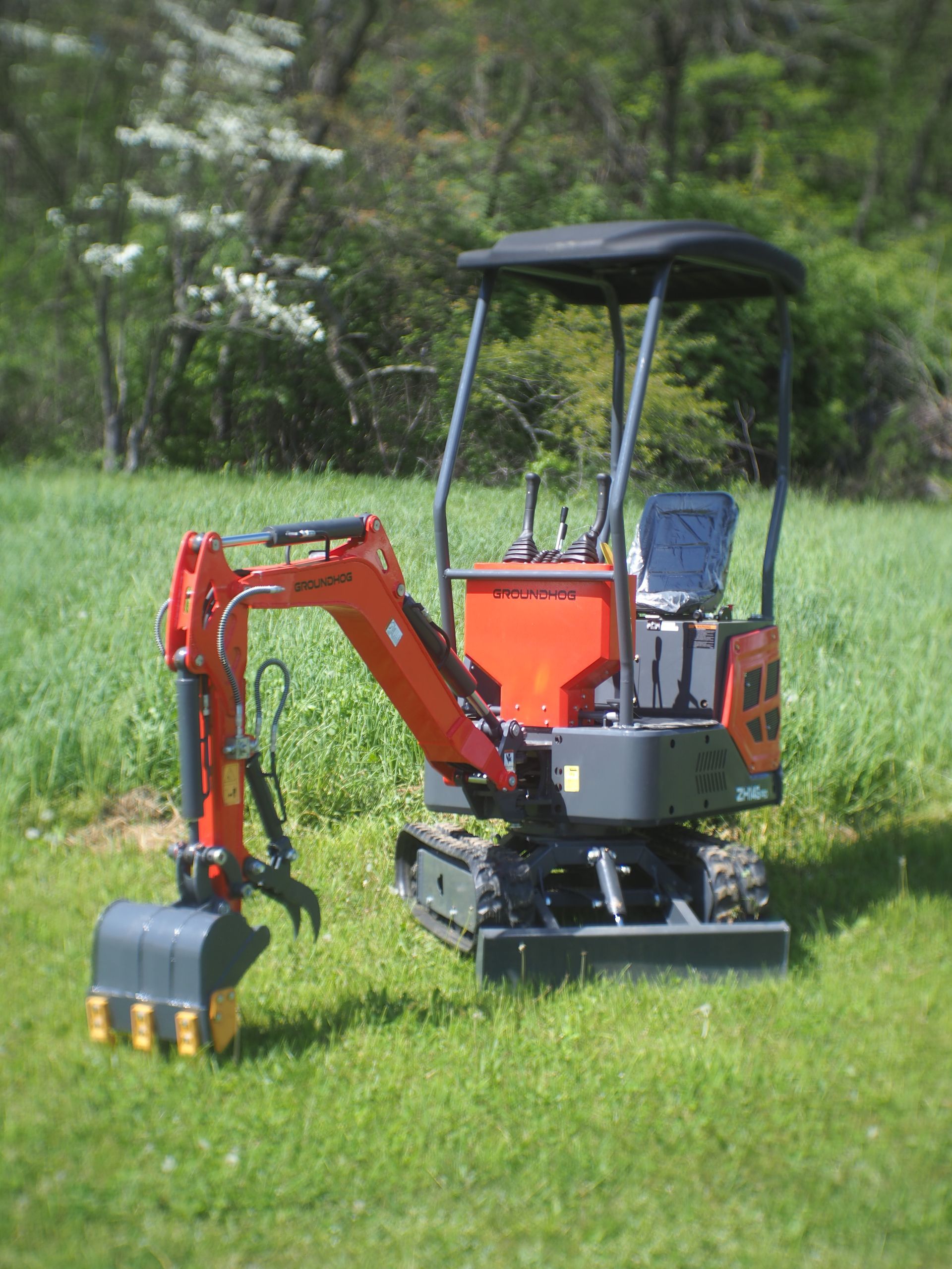 Mini orange excavator on grass, with black canopy and bucket, ready for digging.