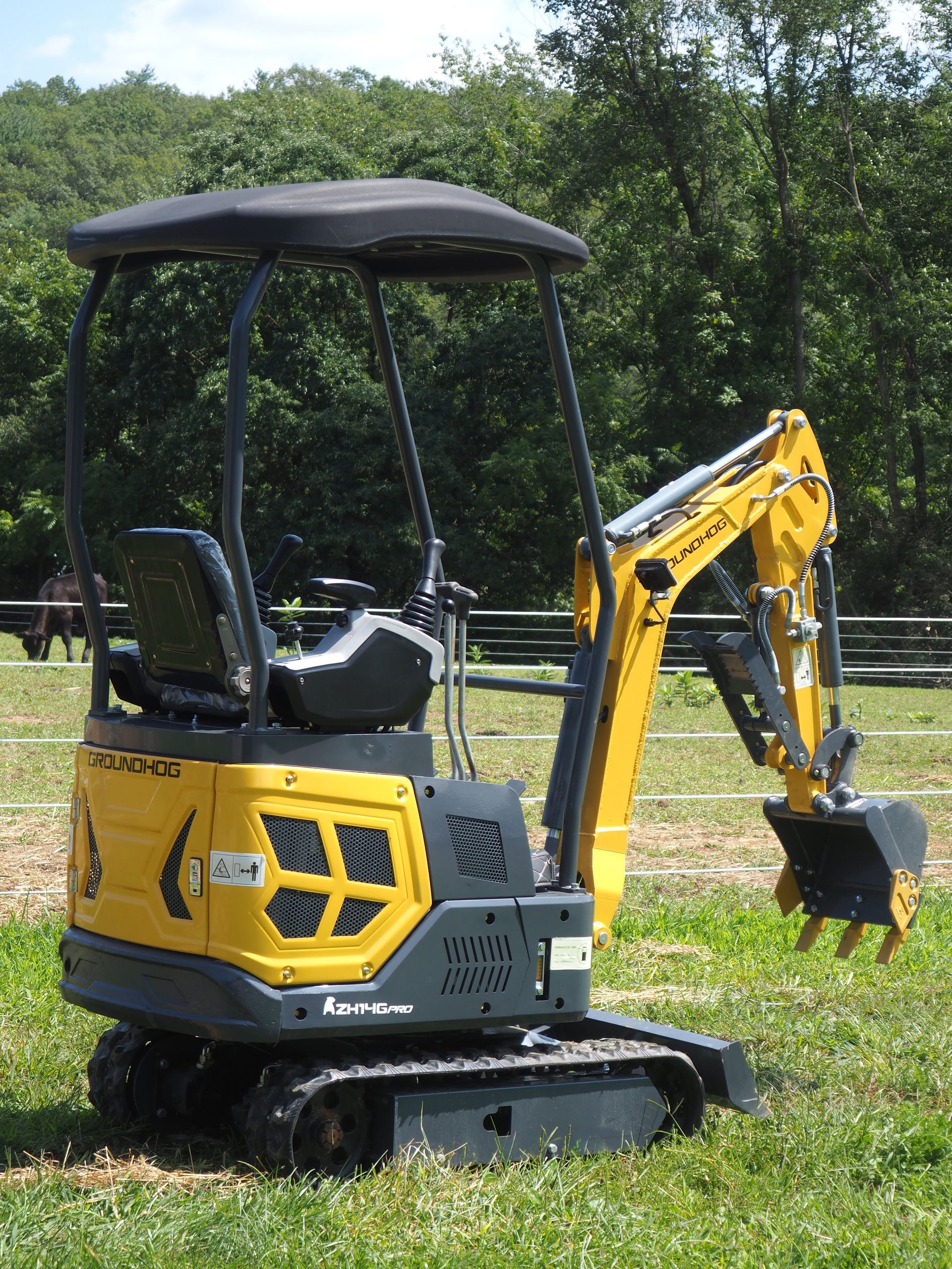 Yellow and gray mini-excavator on tracks in a grassy field.