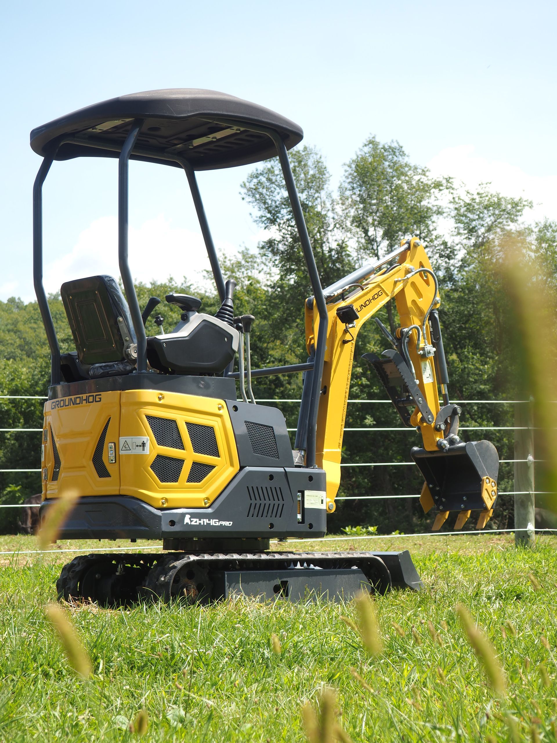 Yellow mini excavator in a grassy field.